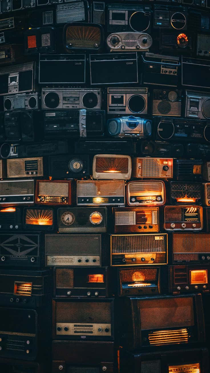 Retro 桌布 壁紙 — 一面密集的復古收音機和手提音響牆，在深色調中散發溫暖的琥珀色光芒。