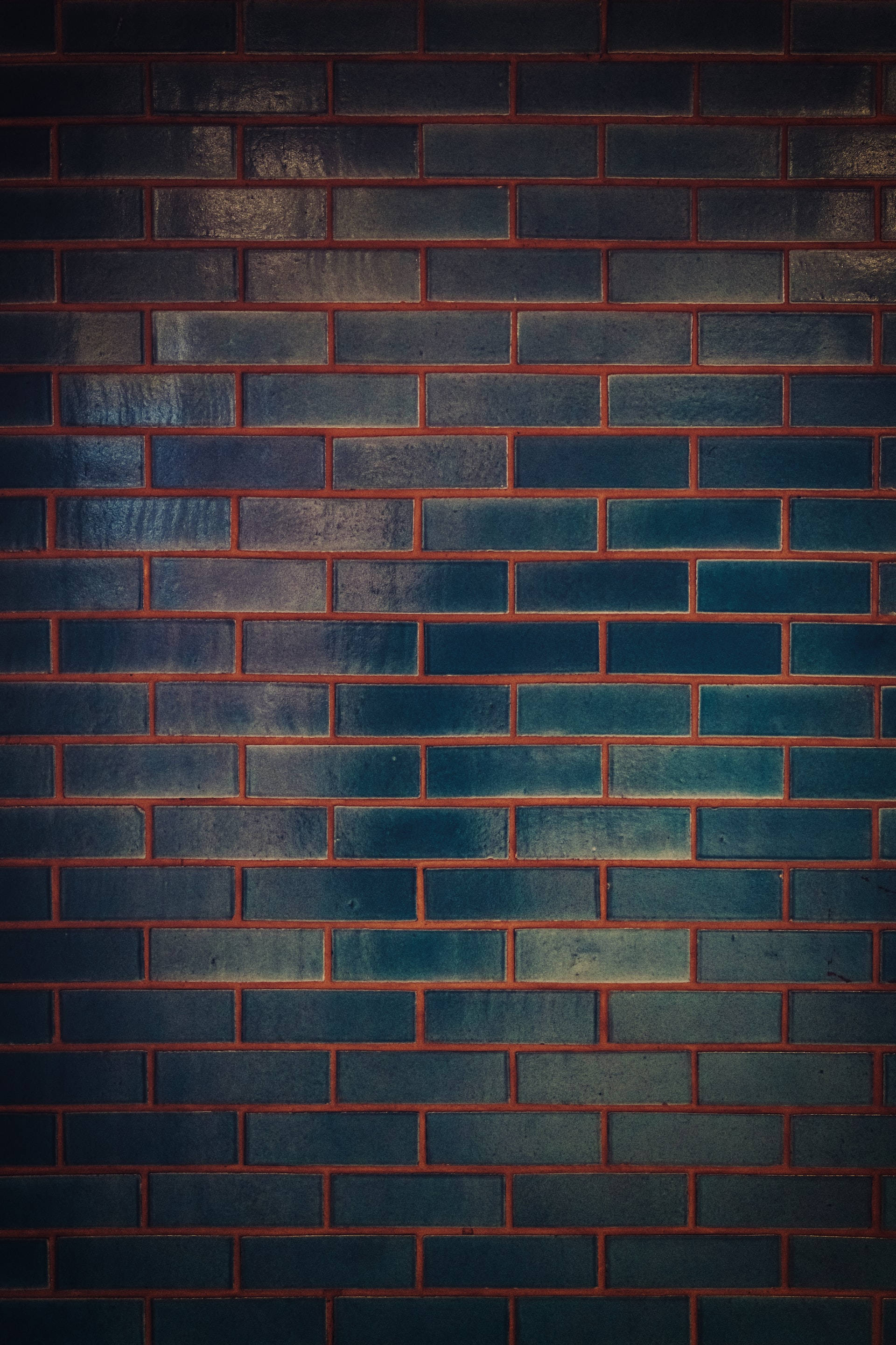 Brick 桌布 壁紙 — 一面帶有紋理的磚牆，深藍色磚塊和溫暖的紅色砂漿在戲劇性的燈光下。
