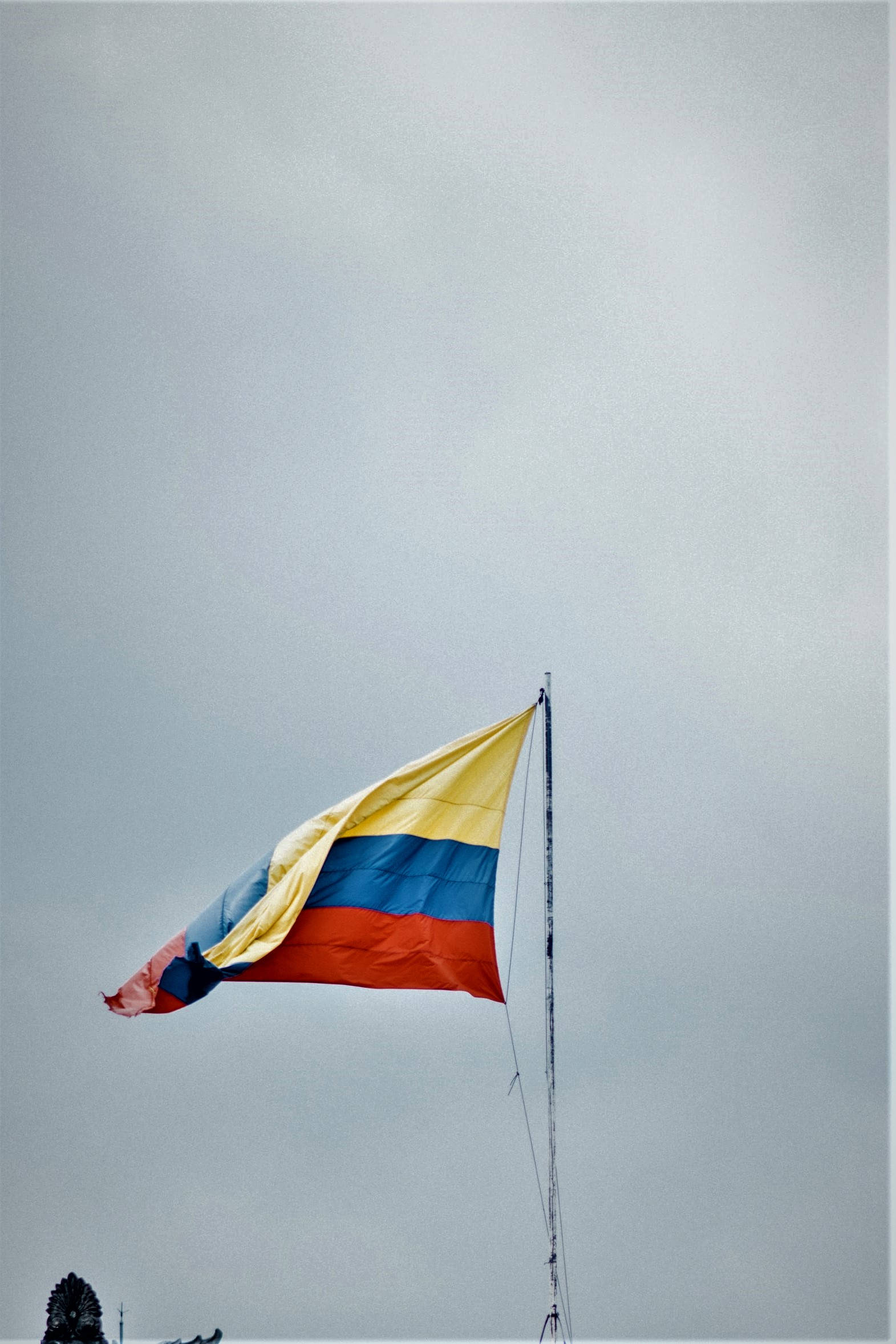 Colombia Flag 桌布 壁紙 — 一面帶有黃、藍、紅條紋的哥倫比亞國旗在柔和的灰色天空中劇烈飄揚。