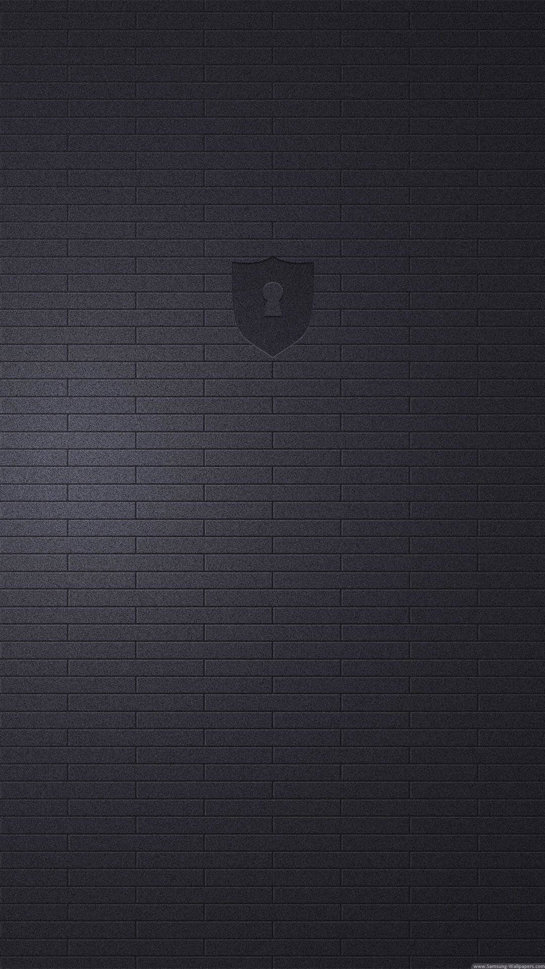 Black Android 桌布 壁紙 — 一面極簡的深色磚牆，中央有一個微妙的浮雕盾牌標誌。