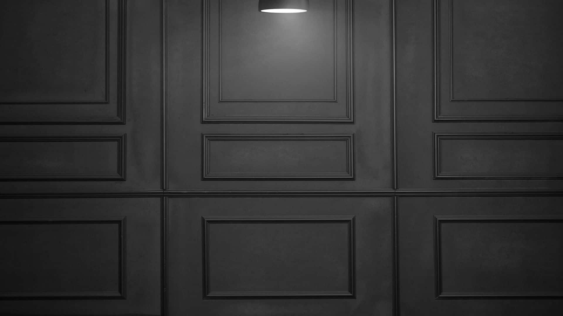 Dark Minimalist 桌布 壁紙 — 一面極簡黑色鑲板牆，由單一頂燈照亮，投射出柔和陰影。