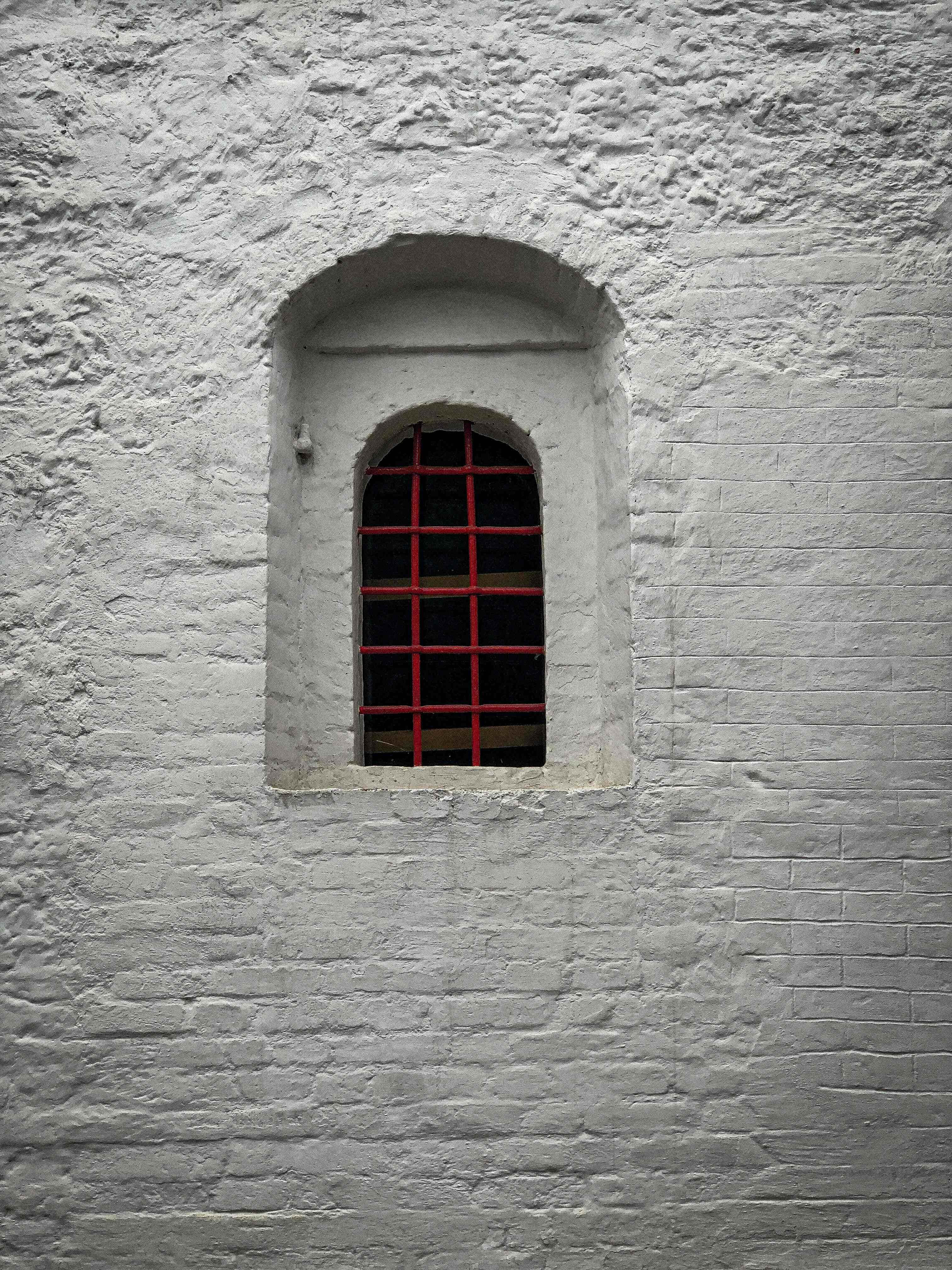 White Brick Wall 桌布 壁紙 — 一面樸素的白磚牆上有一個小拱窗，配以鮮明的紅色金屬欄杆，投射出銳利的陰影。