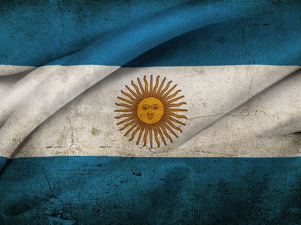 Argentina 桌布 壁紙 — 一面歷經風霜的阿根廷國旗，帶有藍白條紋和金色太陽標誌，在紋理背景上飄揚。