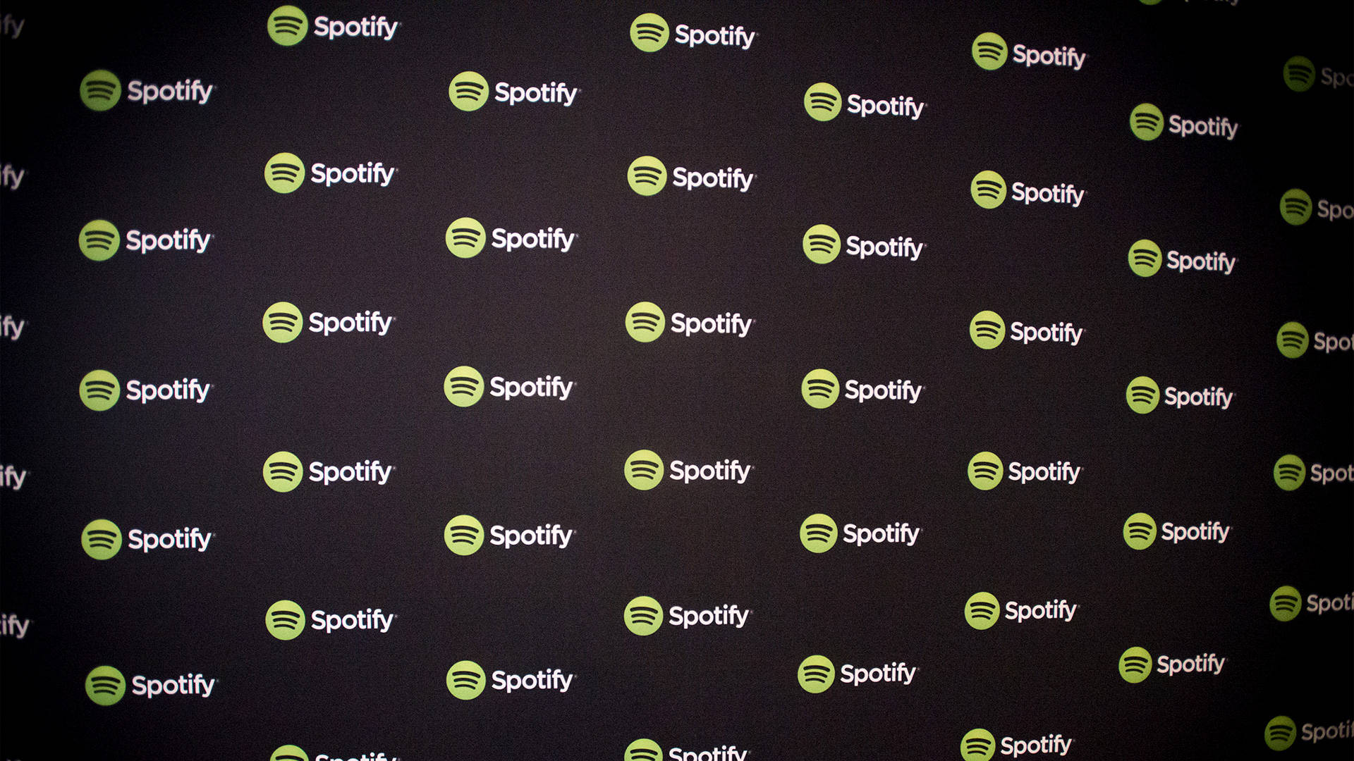 Spotify 桌布 壁紙 — 一面深色牆壁，覆蓋著重複的Spotify標誌，帶有綠色圓圈和白色文字。