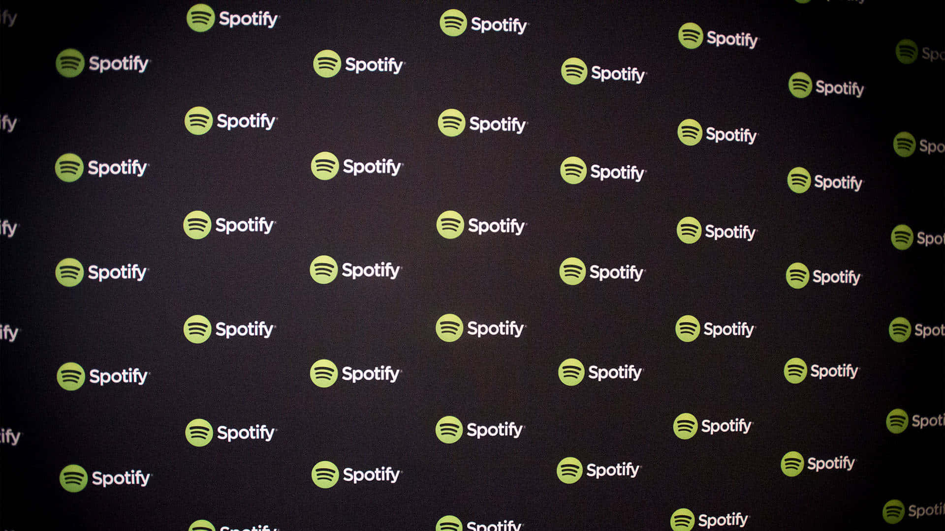 Spotify 桌布 壁紙 — 一面深色牆壁覆蓋著重複的綠色和白色Spotify標誌，形成品牌圖案。