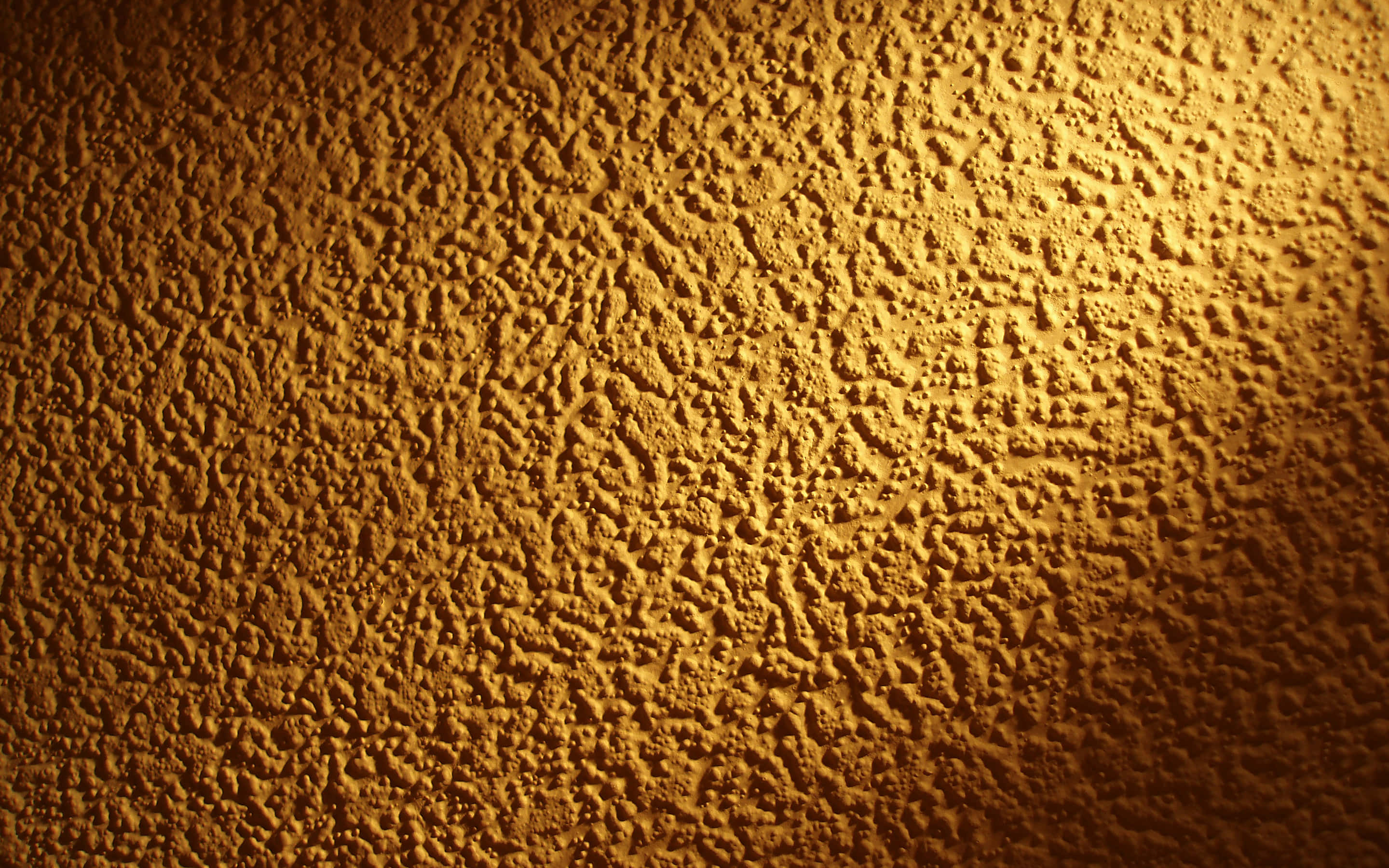 Yellow Grunge 桌布 壁紙 — 一面溫暖照明的紋理牆，帶有金色琥珀色調和深邃陰影，營造出舒適親密的氛圍。