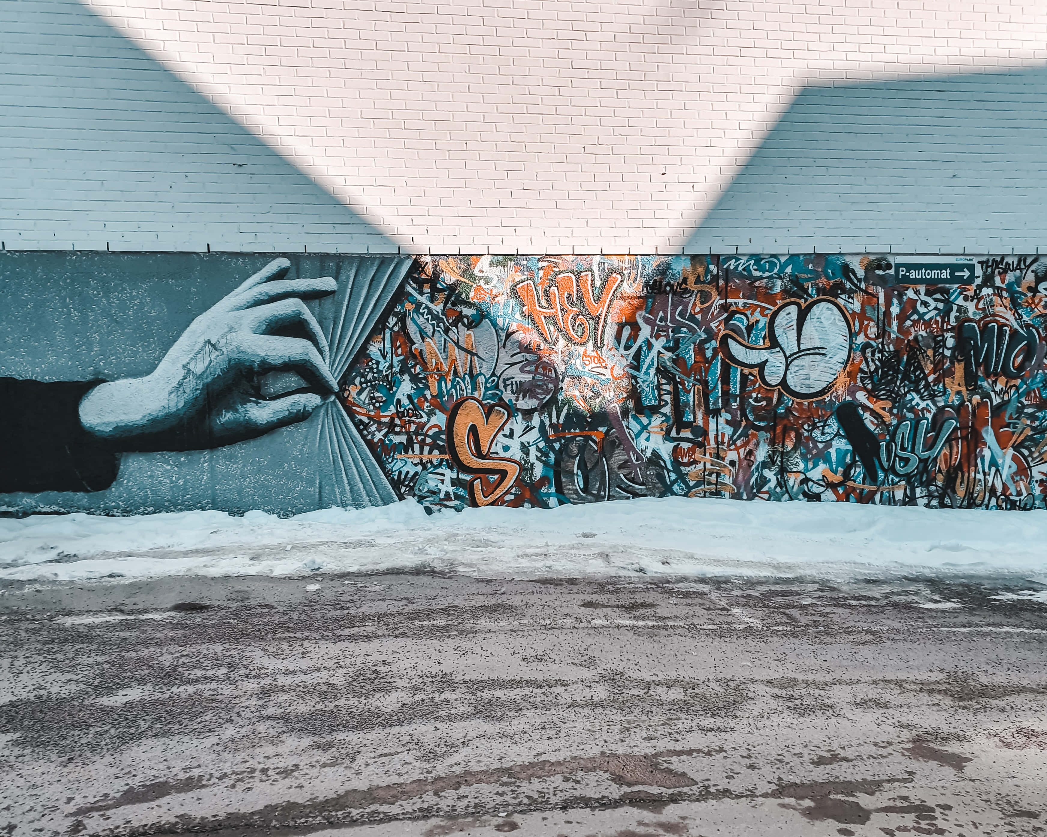 Wall Painting 桌布 壁紙 — 一面純白磚牆上有一幅大型壁畫，描繪一隻手拉開窗簾，露出雪地下混亂的塗鴉。