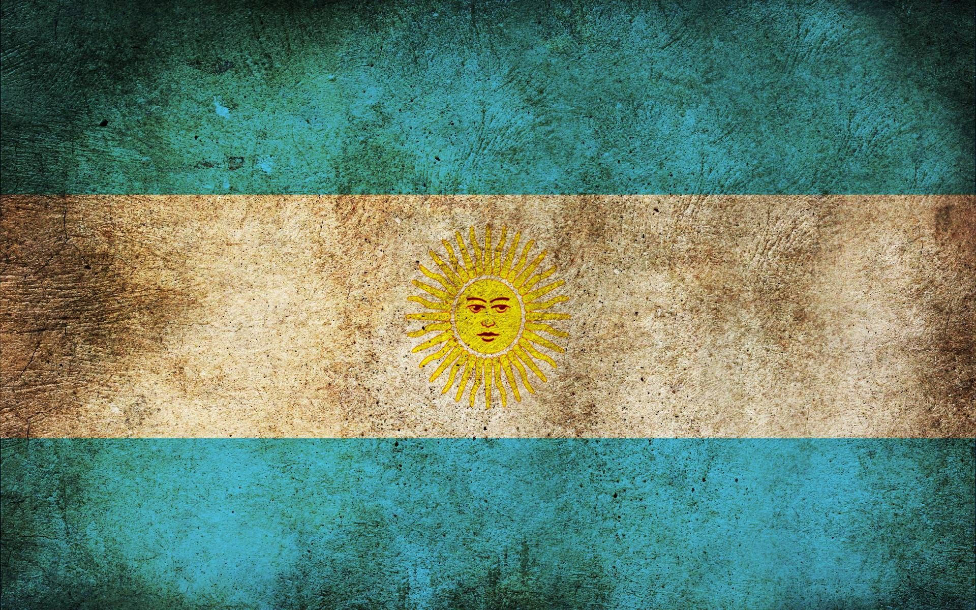 Argentina 桌布 壁紙 — 一面經過風化的阿根廷國旗，帶有藍、白、金色條紋和太陽標誌，顯示出質感和歲月痕跡。