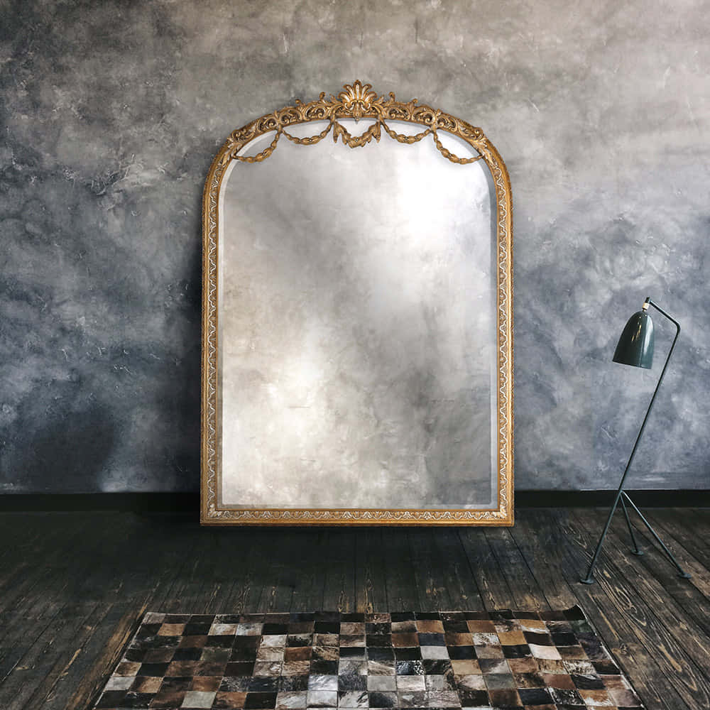 mirror 桌布 壁紙 — 一面華麗的金框鏡子靠著紋理灰色牆壁，旁邊有一盞現代黑色落地燈在深色木地板上。