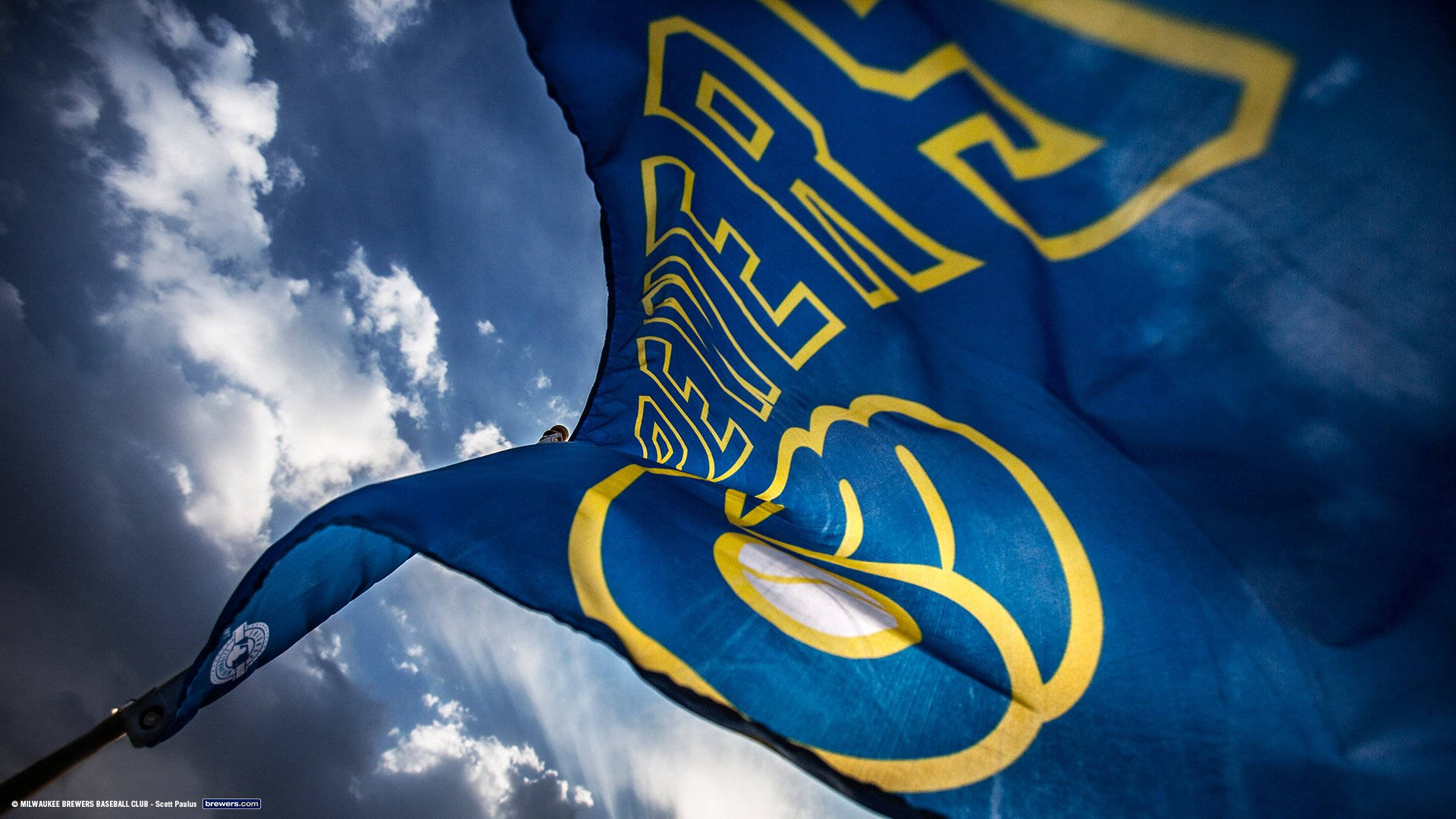 Brewers 桌布 壁紙 — 一面藍黃色的聖路易斯藍調旗幟在戲劇性的多雲天空下動態飄揚。