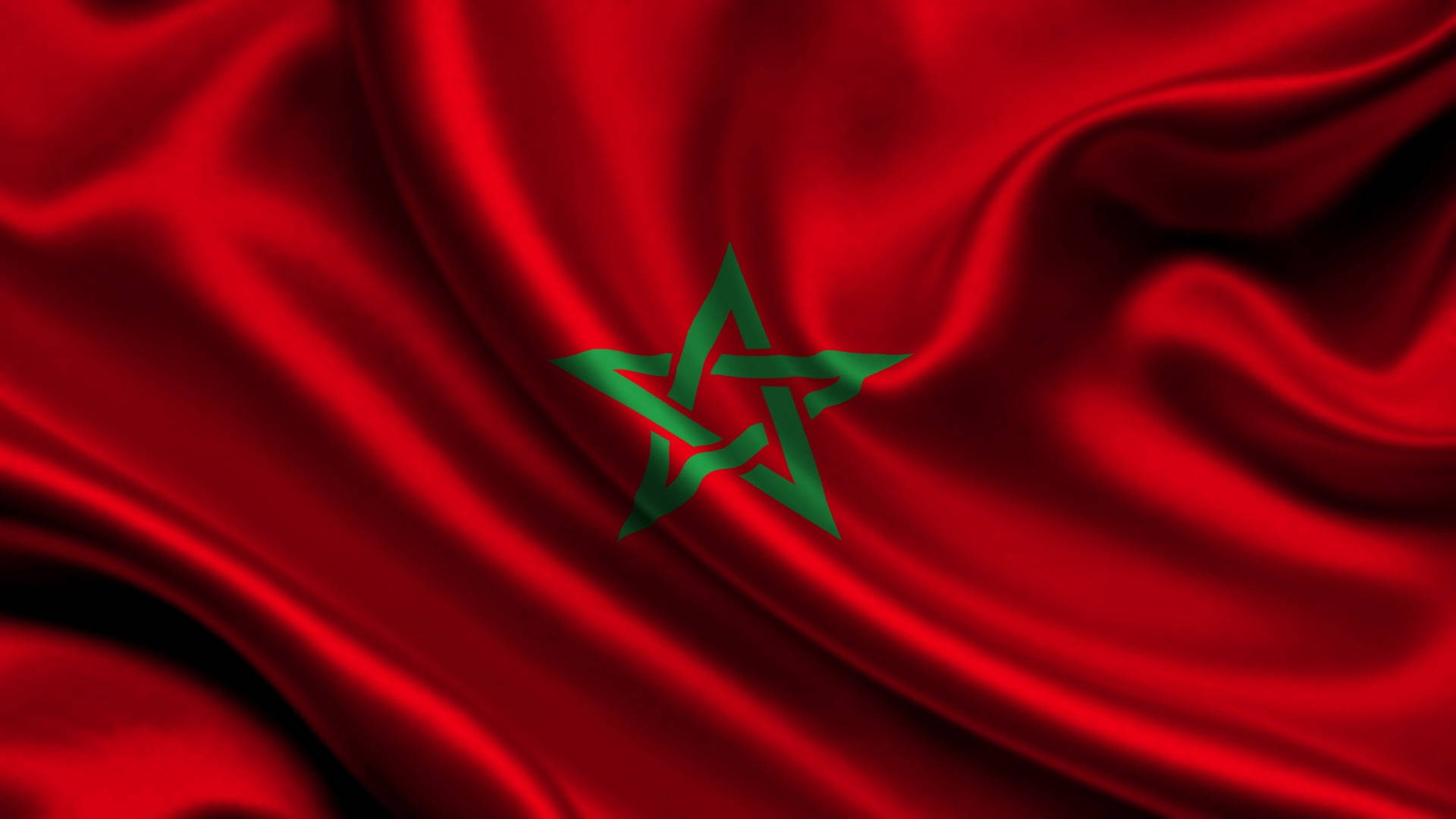 Morocco 桌布 壁紙 — 一面豐富的紅色摩洛哥國旗，中央有綠色五角星，在戲劇性的燈光下以柔軟的褶皺動態飄動。