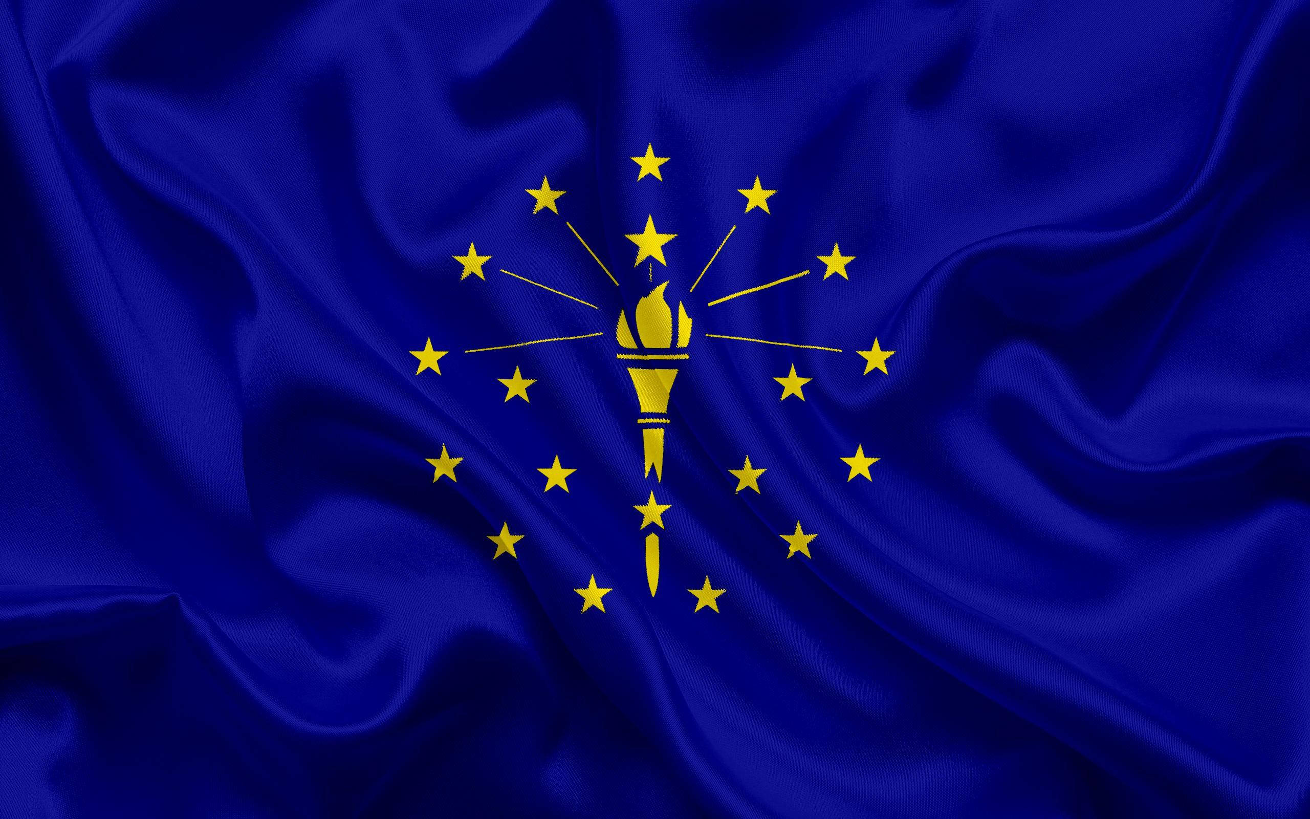 Indiana 桌布 壁紙 — 一面豐富的藍色旗幟，帶有金色星星和火炬標誌，在風中動態飄揚。