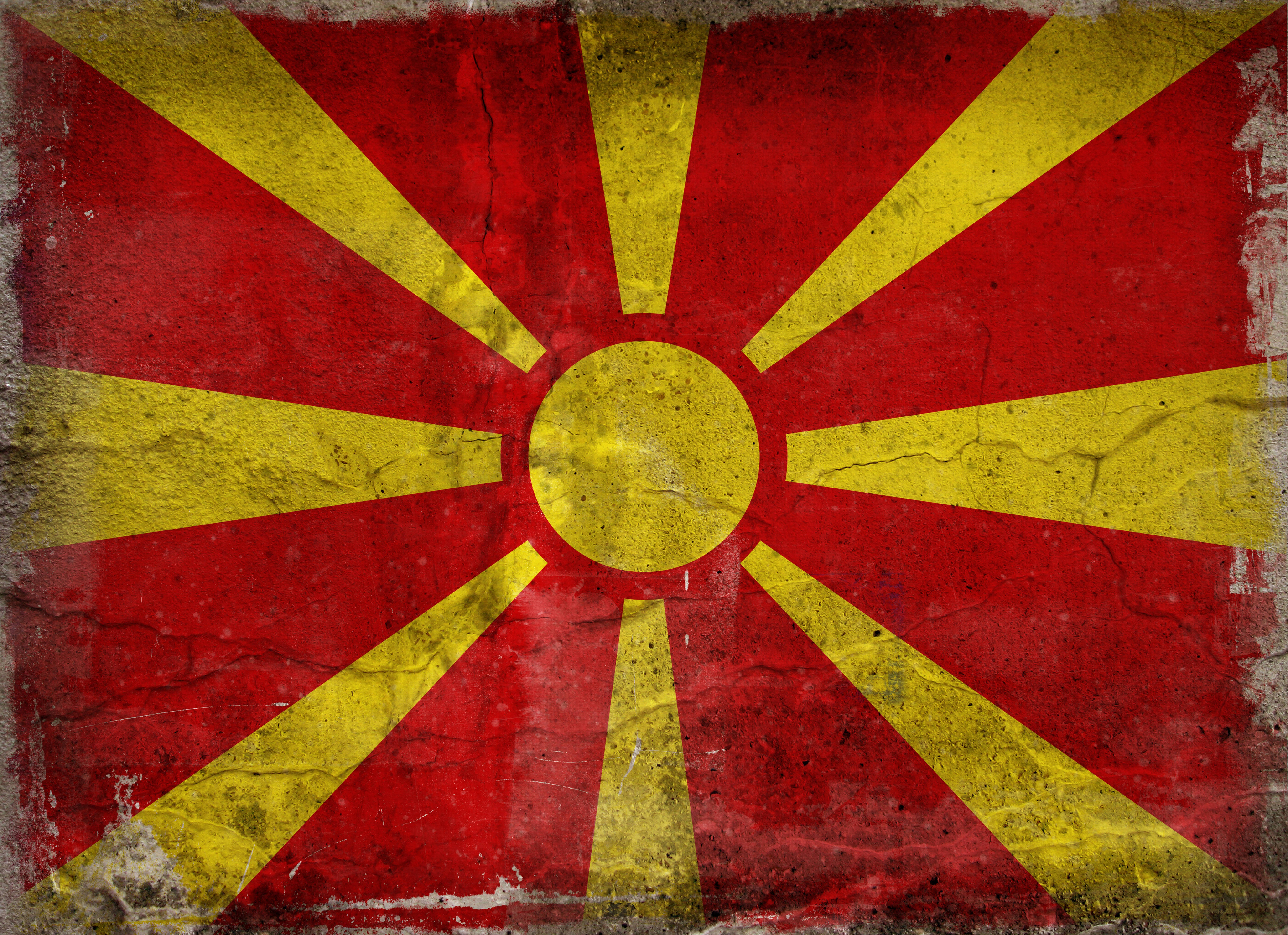 Macedonia 桌布 壁紙 — 一面風化且破裂的北馬其頓國旗，在紋理背景上呈現大膽的紅黃色太陽光芒設計。