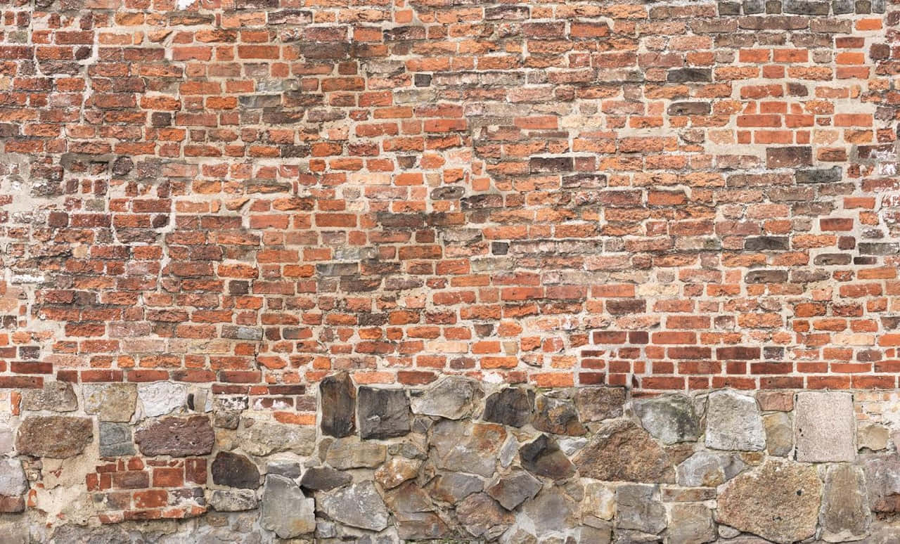 wall 桌布 壁紙 — 一面風化的磚牆，帶有石頭地基，在自然光下展現出質樸的紋理和溫暖的大地色調。