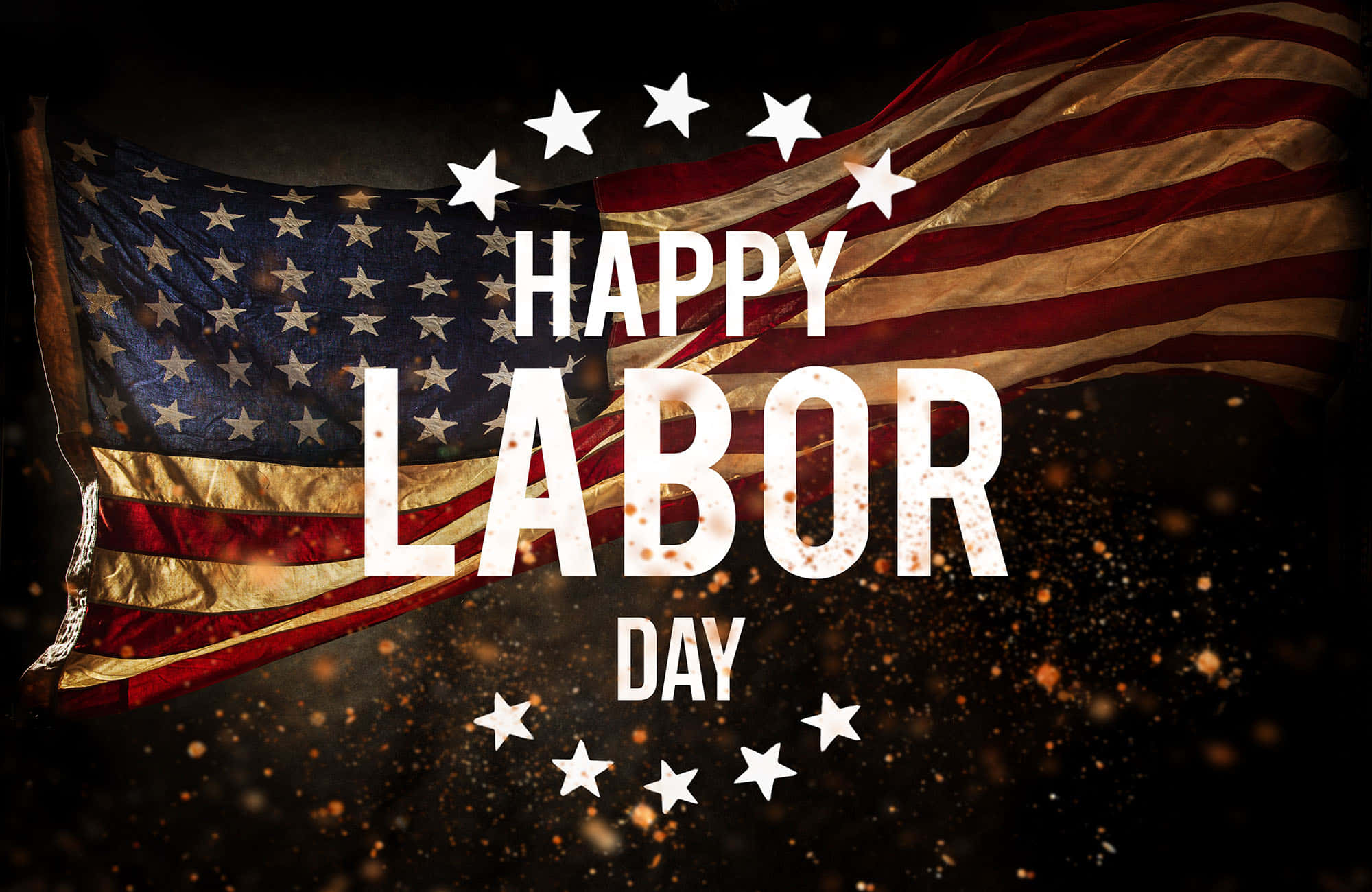 勞動節 桌布 壁紙 — 一面風化的美國國旗在粗體白色文字「HAPPY LABOR DAY」後面飄揚，文字周圍環繞著星星和金色火花，背景為深色。