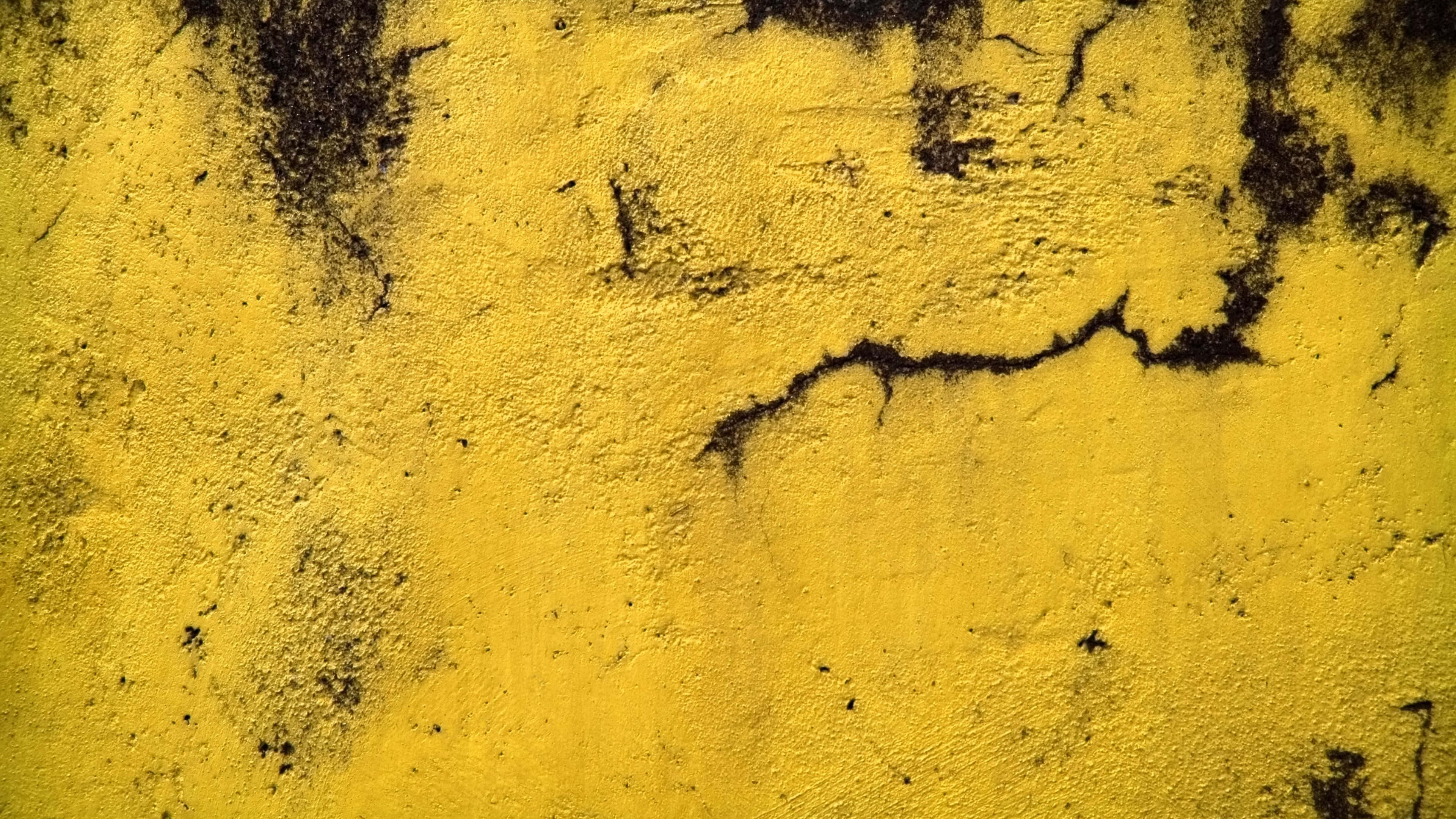 Yellow Grunge 桌布 壁紙 — 一面風化的黃色牆壁，帶有深色裂紋和紋理表面，顯示出老化和磨損的跡象。
