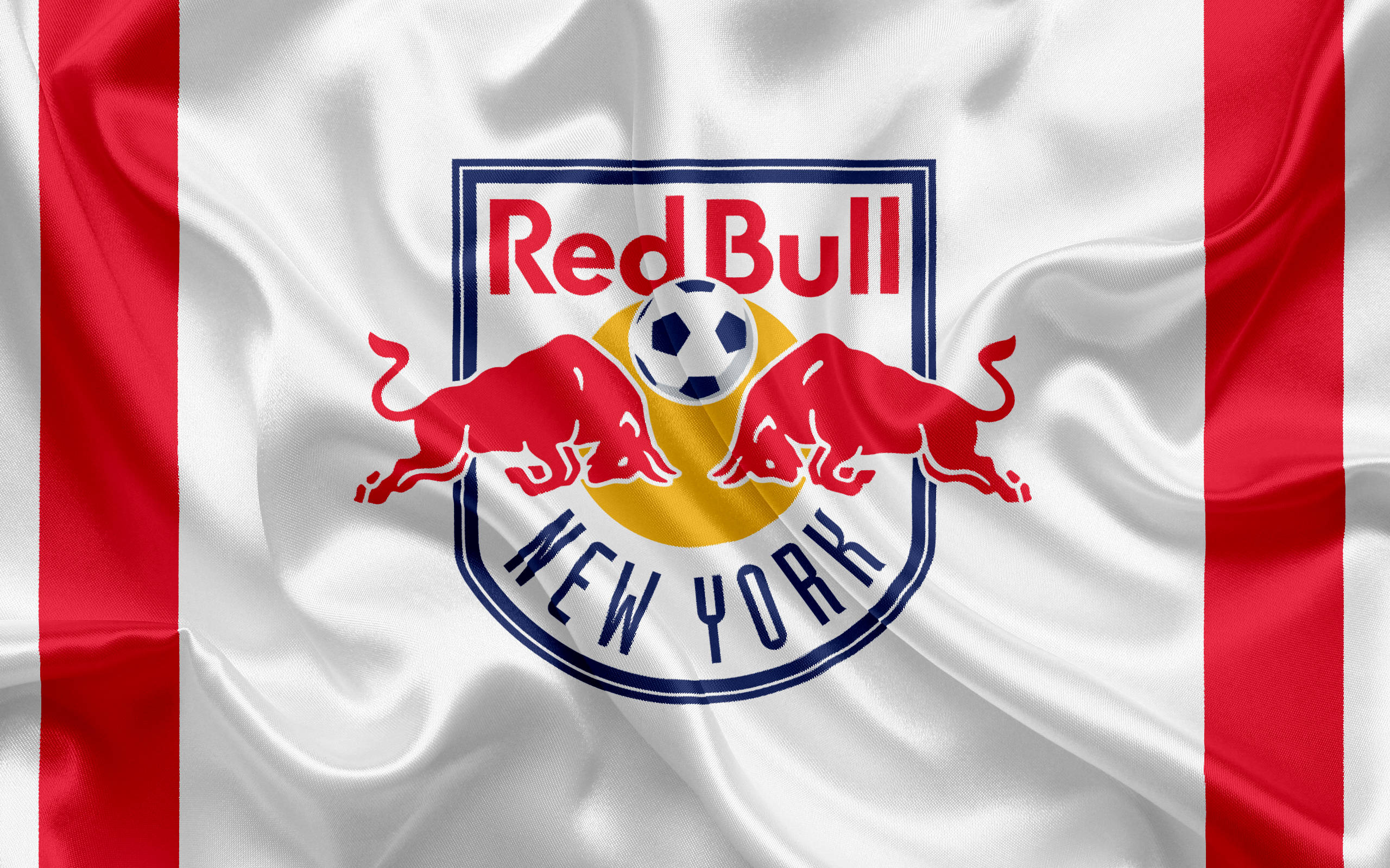 Red Bull 桌布 壁紙 — 一面飄揚的紅白旗幟，上面有 Red Bull New York 足球隊的標誌，包含兩頭衝鋒的公牛和一個足球。