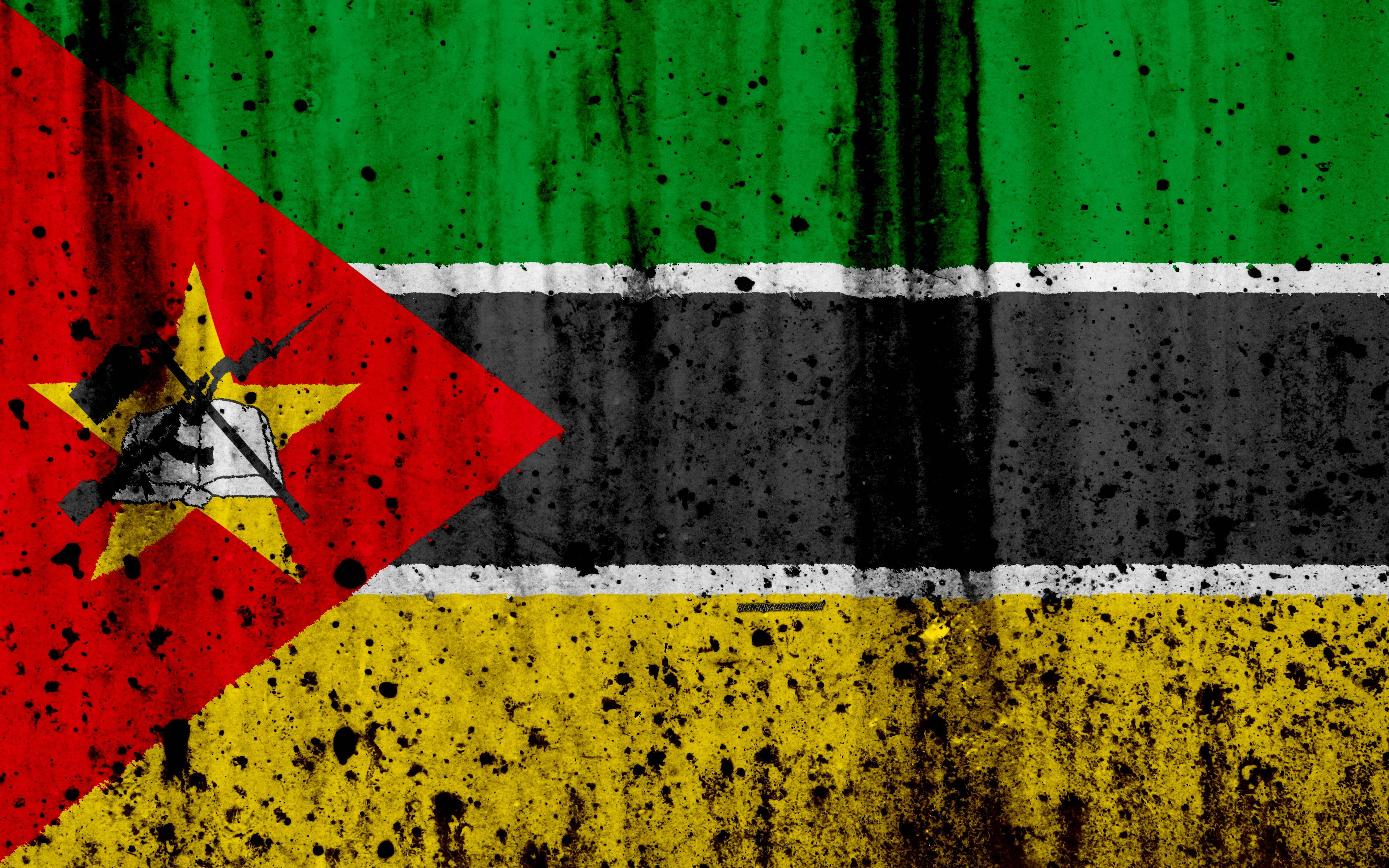 Mozambique 桌布 壁紙 — 一面飽經風霜的莫三比克國旗，帶有黑色油漆飛濺和紋理布料，顯示綠色、黑色、黃色條紋和帶有星星和步槍的紅色三角形。