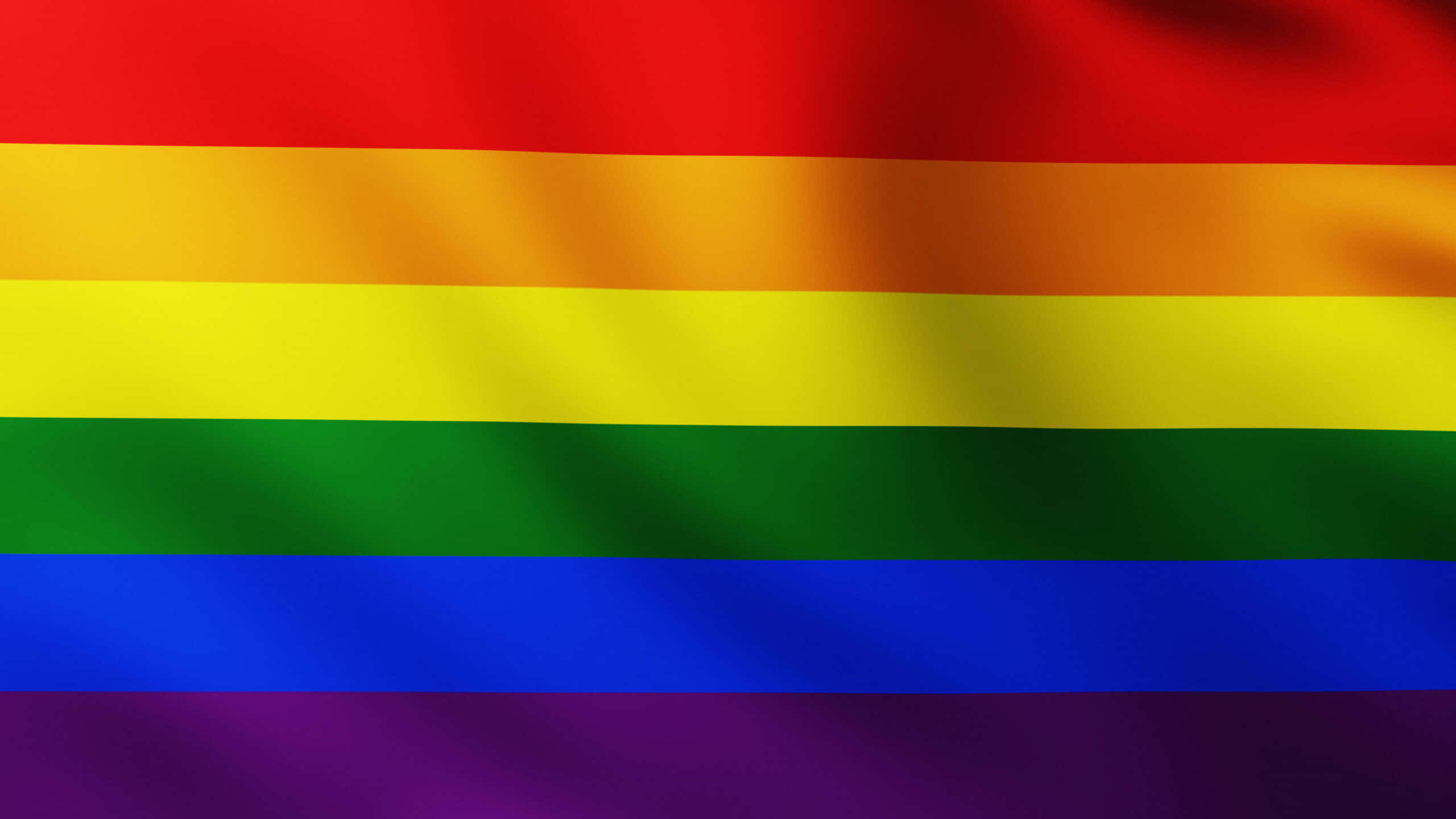 Pride Flag 桌布 壁紙 — 一面鮮豔的彩虹旗在動態中飄揚，柔軟的褶皺在其大膽的水平條紋上捕捉光線。