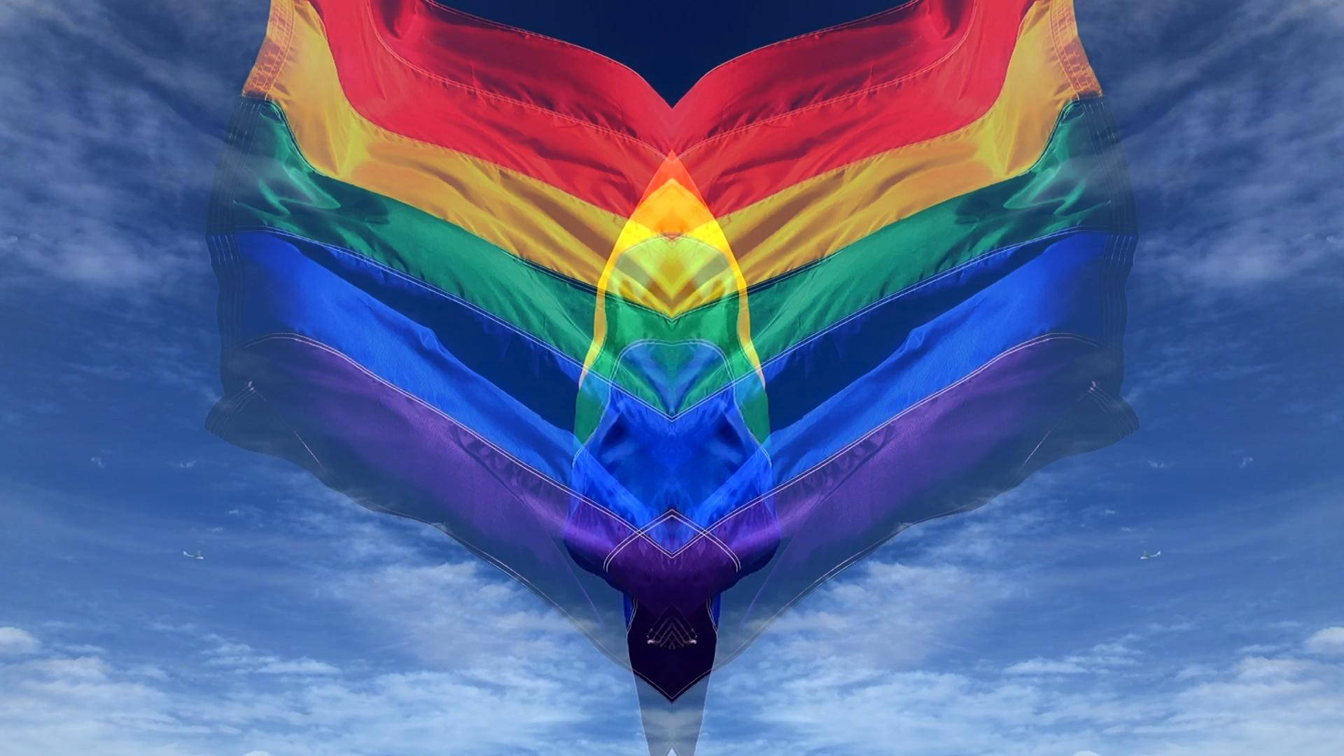 Pride Flag 桌布 壁紙 — 一面鮮豔的彩虹旗在晴朗的藍天和白雲中戲劇性地飄揚。