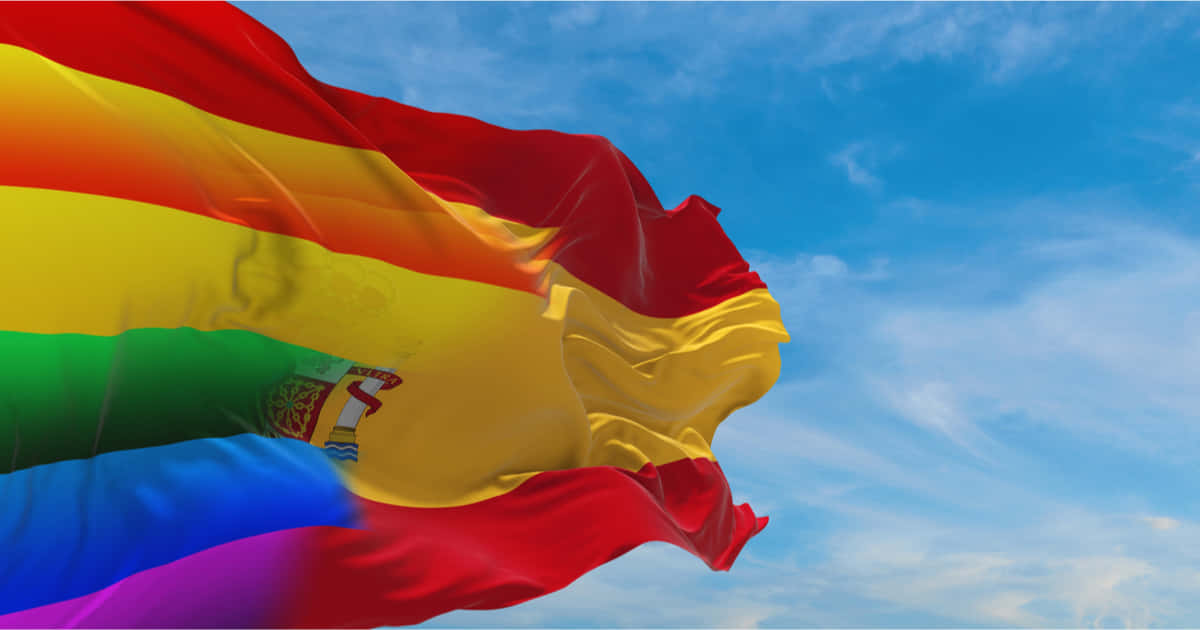 Flag 桌布 壁紙 — 一面鮮豔的彩虹旗帶有西班牙國徽，在藍天白雲中飄揚。