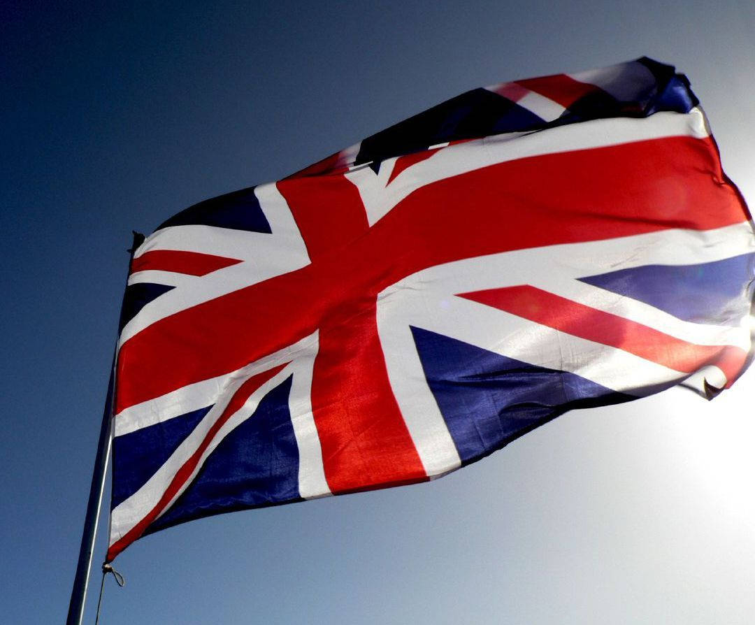 United Kingdom Flag 桌布 壁紙 — 一面鮮豔的英國國旗在晴朗的藍天下，在明亮的陽光中動態飄揚。
