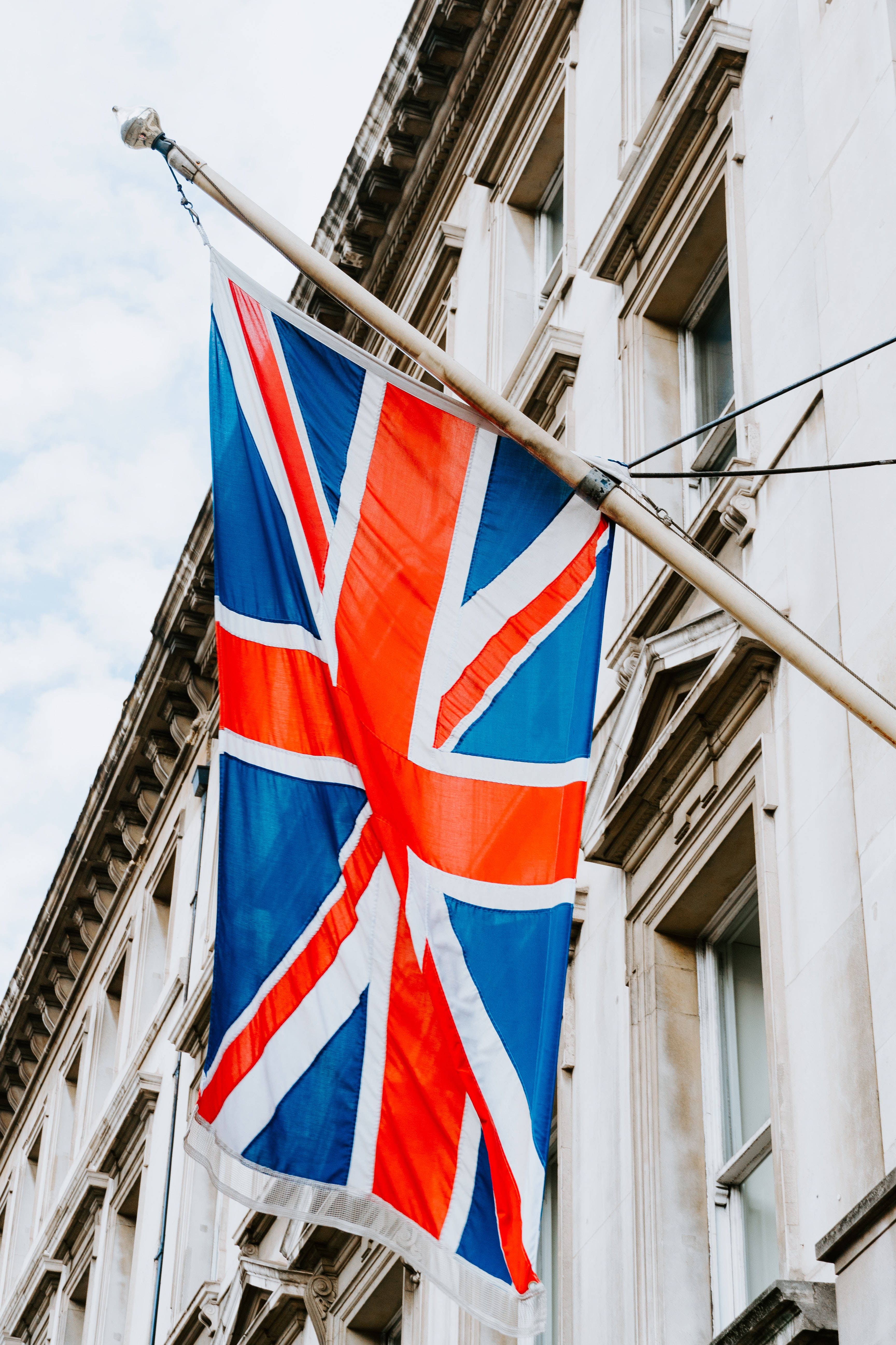 England 桌布 壁紙 — 一面鮮豔的英國國旗在陰天中自豪地飄揚，掛在經典白色建築外牆的旗桿上。