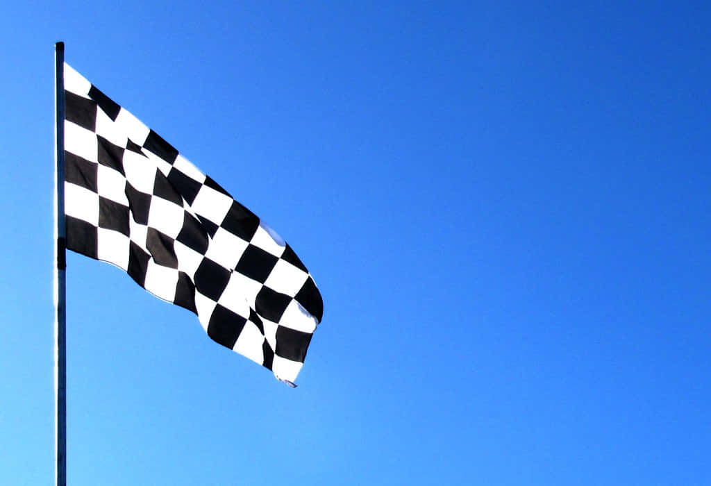 Chequered Flag 桌布 壁紙 — 一面黑白格子賽車旗在晴朗的藍天下動態飄揚。