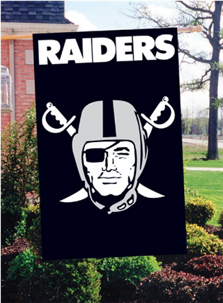 突襲者 桌布 壁紙 — 一面黑色的Raiders旗幟，上面有白色頭盔戰士和交叉的劍，掛在磚房附近的綠色庭院中。
