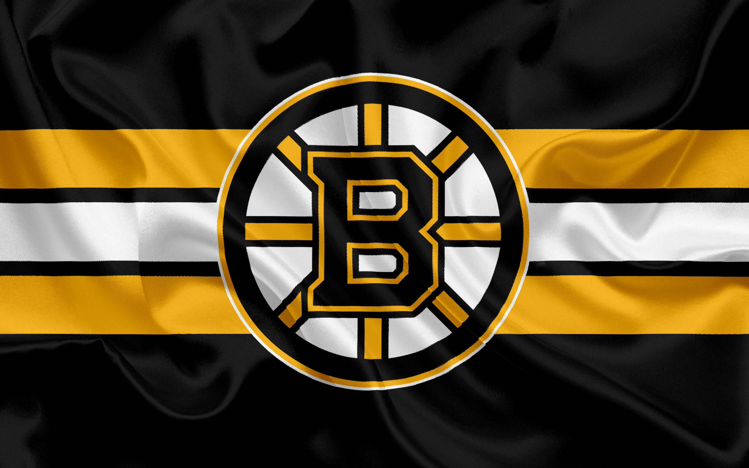 bruins 桌布 壁紙 — 一面黑色緞面旗幟，帶有鮮明的黃色、白色和黑色條紋，中央有一個圓形標誌，上面有一個風格化的字母B。