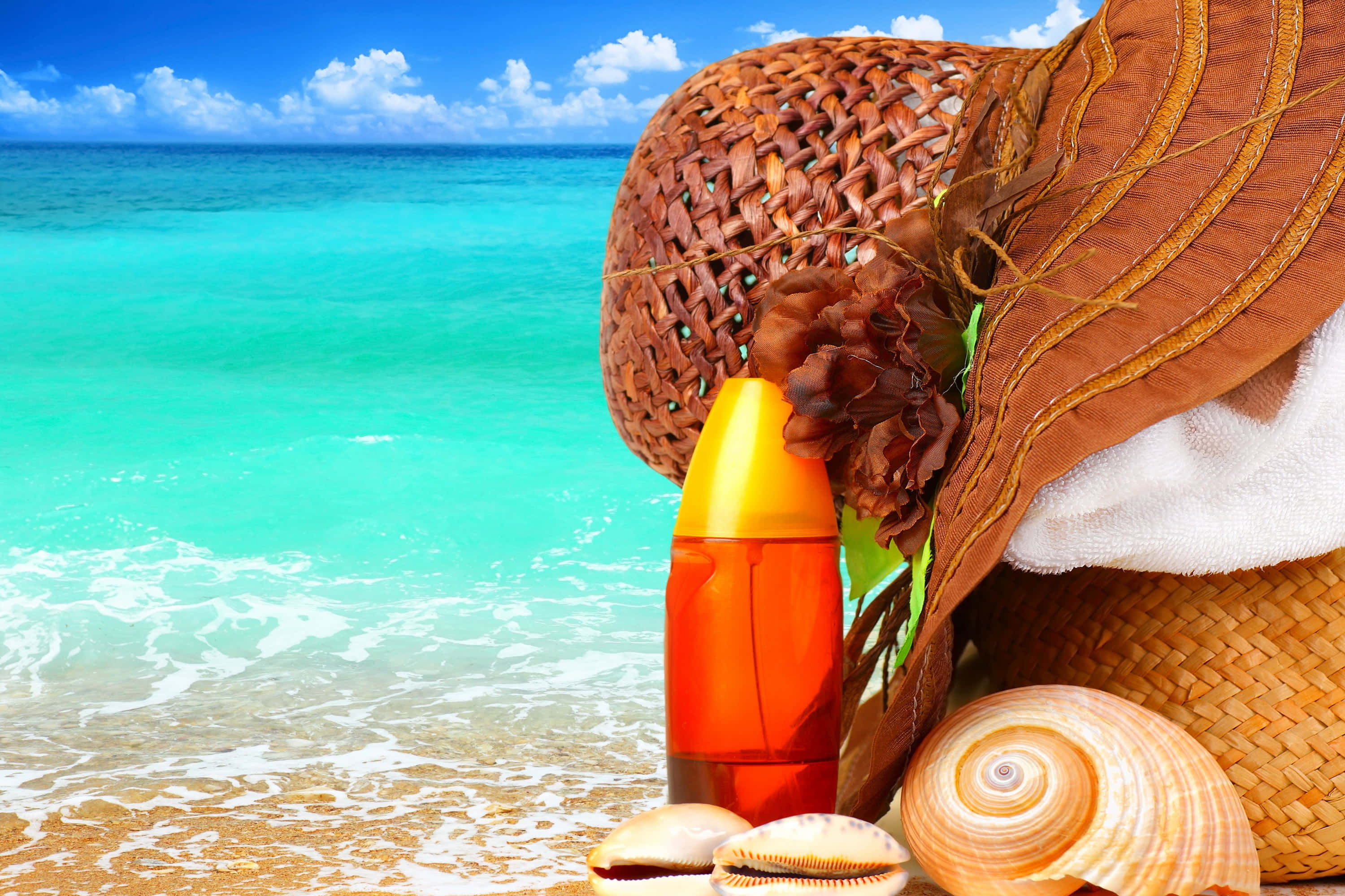 Beach Bag 桌布 壁紙 — 一頂太陽帽、防曬乳瓶和貝殼放在金色沙灘上，旁邊是碧綠的海浪，上方是明亮的藍天。
