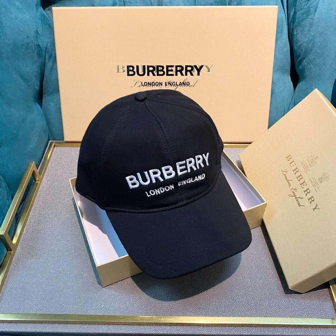 Burberry 桌布 壁紙 — 一頂帶有白色標誌的黑色Burberry帽子優雅地放在一個米色盒子裡，置於金色邊緣的托盤上，背景是藍綠色天鵝絨。