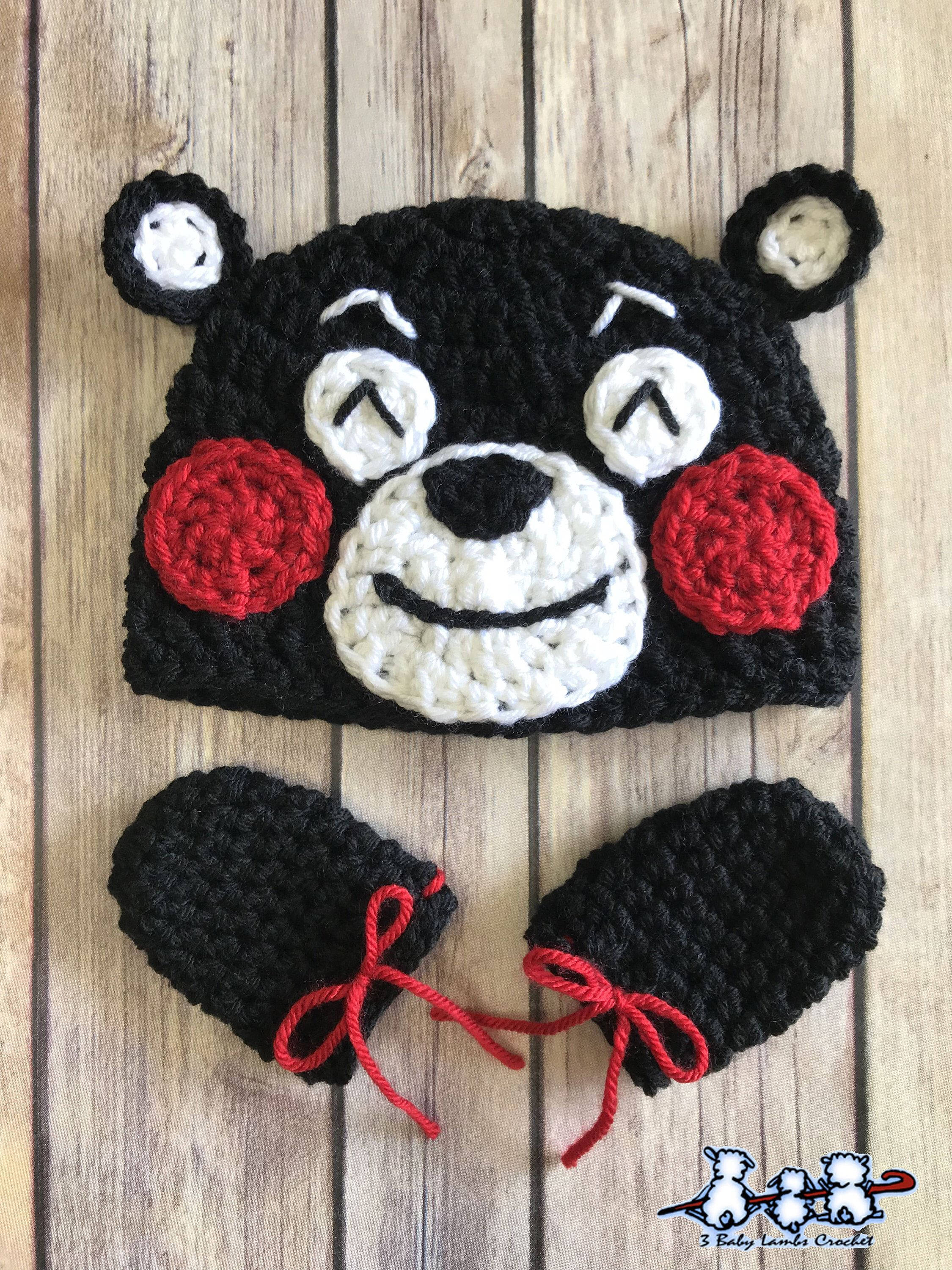 熊本熊 桌布 壁紙 — 一頂手工製作的黑色鉤針編織熊帽，配有紅色臉頰和相配的連指手套，放在木質表面上。