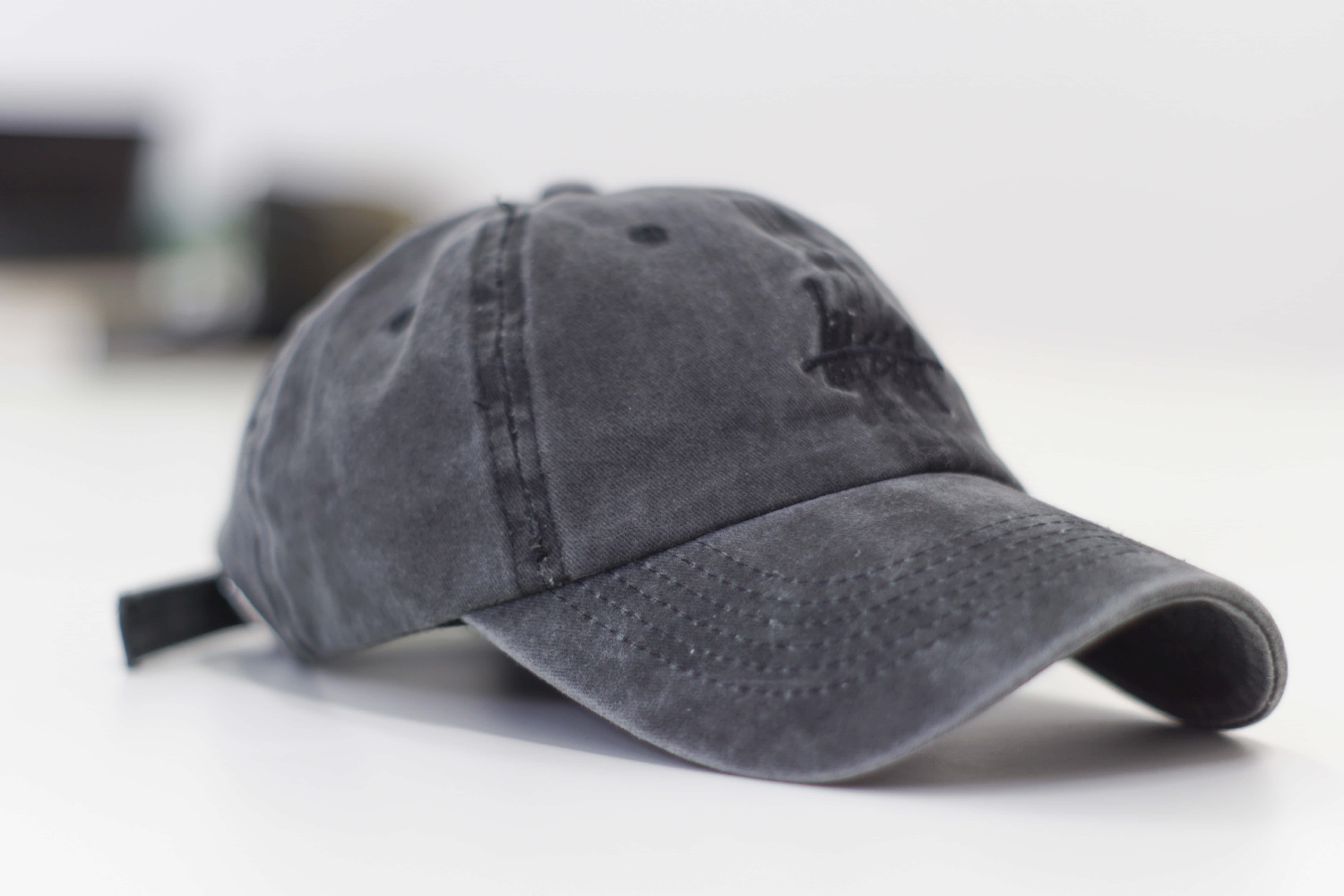 Cap 桌布 壁紙 — 一頂深灰色仿舊棒球帽，帶有精緻刺繡標誌，放置在潔白表面上。