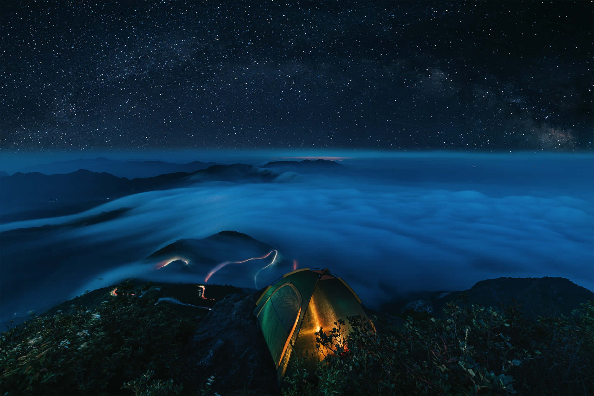 Camp 桌布 壁紙 — 一頂發光的帳篷坐落在山頂上，下方是雲海，上方是繁星點點的夜空。