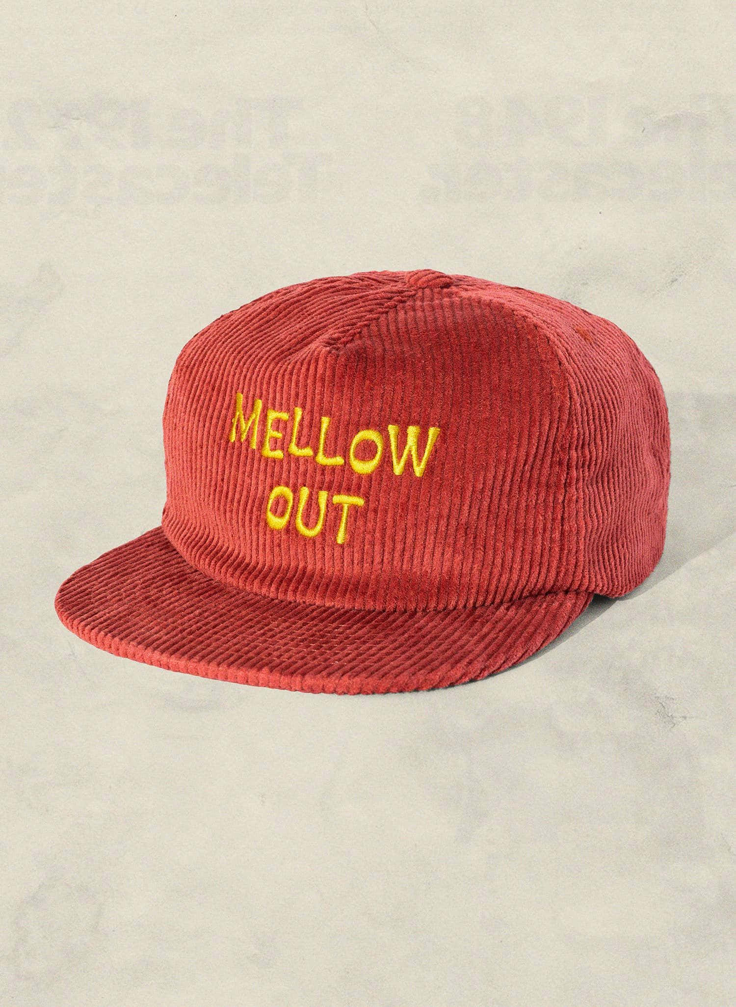 Hat 桌布 壁紙 — 一頂紅色燈芯絨帽，上面有黃色 'MELLOW OUT' 刺繡，放在淺灰色紋理表面上。