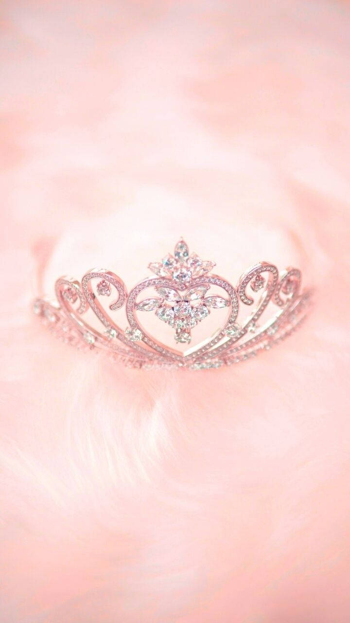 queen girly 桌布 壁紙 — 一頂閃閃發光的銀色頭飾，鑲嵌著鑽石，優雅地放置在柔軟的粉紅色毛絨表面上。