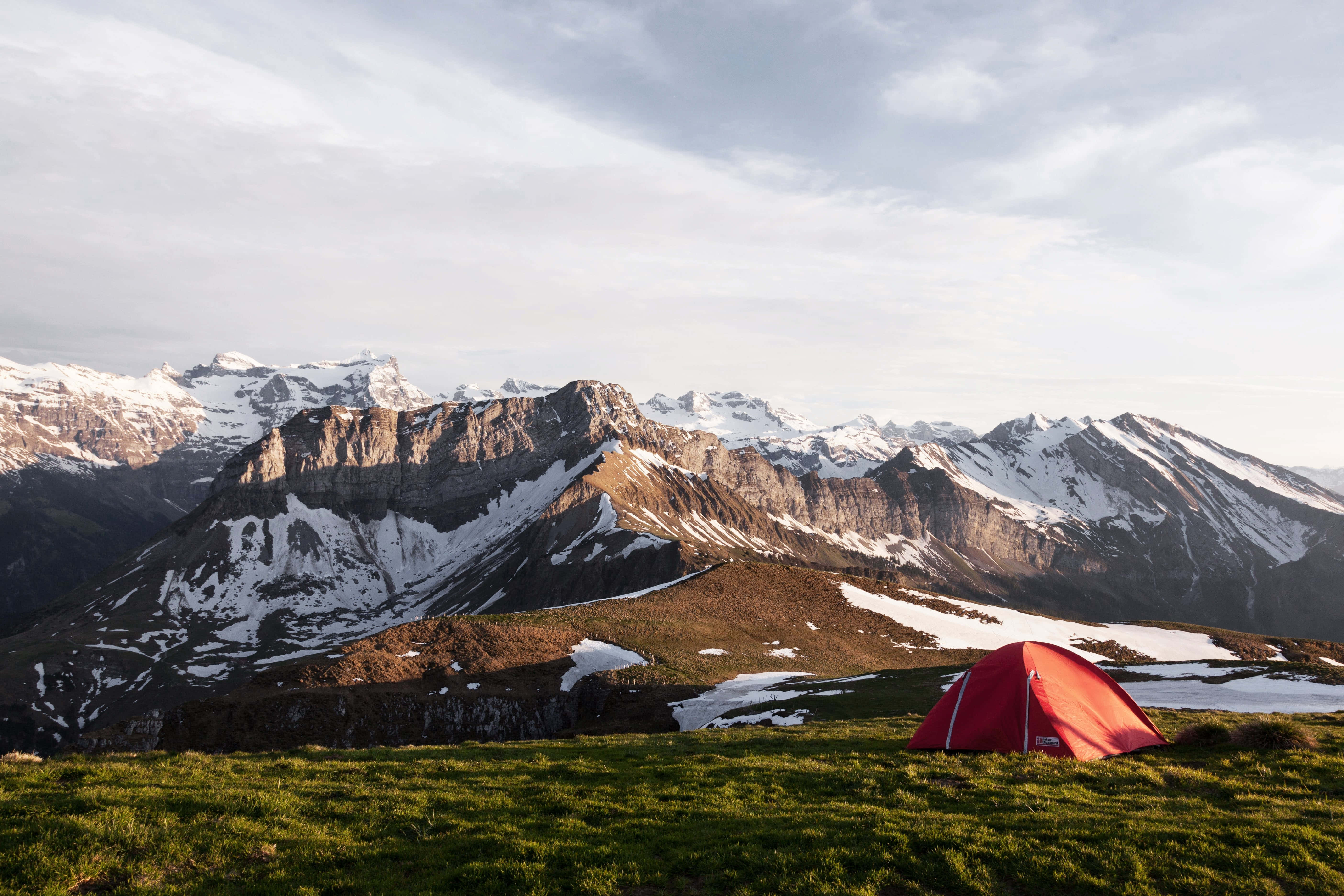 Camping 桌布 壁紙 — 一頂鮮紅色的帳篷坐落於陽光明媚的草地上，背景中白雪覆蓋的山脈巍峨聳立。