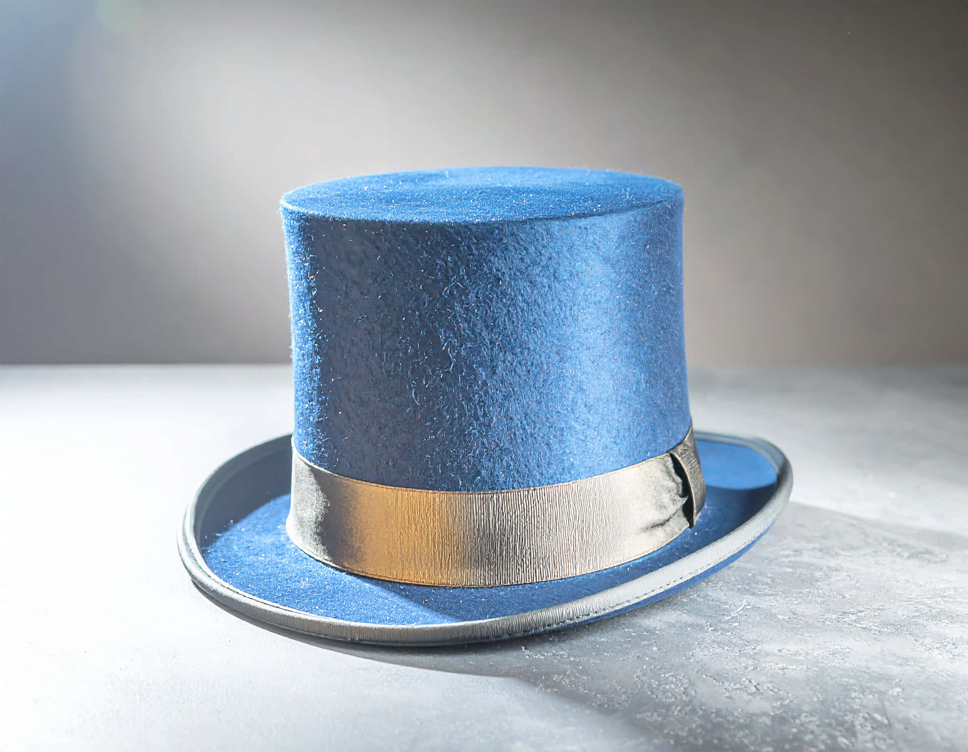 Velvet Hat 壁紙 — 一頂鮮藍色氈帽，配有金屬金色帶子，在柔和的工作室燈光下，放置在帶紋理的灰色表面上。