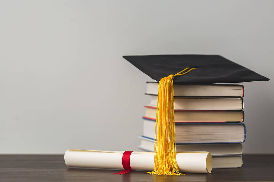 Education 桌布 壁紙 — 一頂黑色畢業帽配金色流蘇，放在木質表面上的一疊書本上，旁邊有一卷畢業證書。