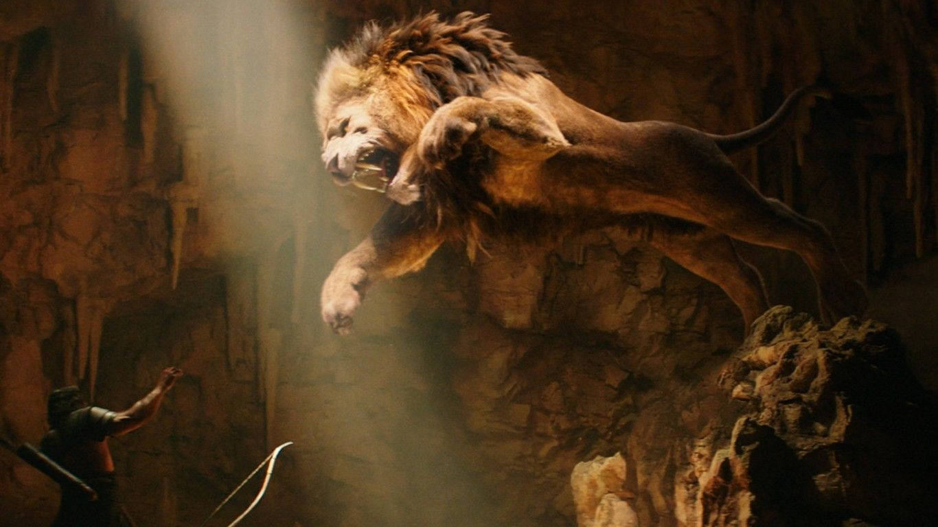 獅子 桌布 壁紙 — 一頭雄獅從岩石懸崖躍向一個孤獨的弓箭手，在一個塵土飛揚的洞穴中，只有一束光照亮。