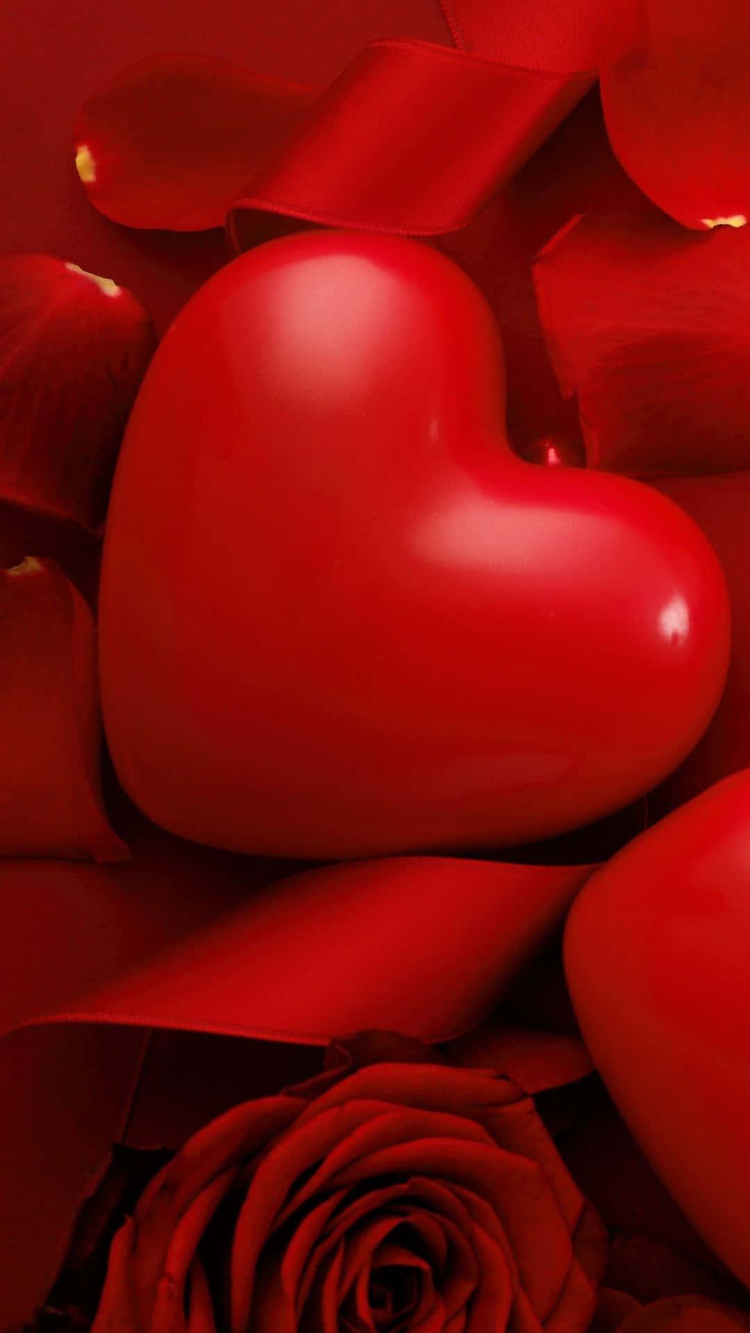Rose Heart 桌布 壁紙 — 一顆亮麗的紅色心形躺在散落的玫瑰花瓣和一朵盛開的深紅玫瑰之間。