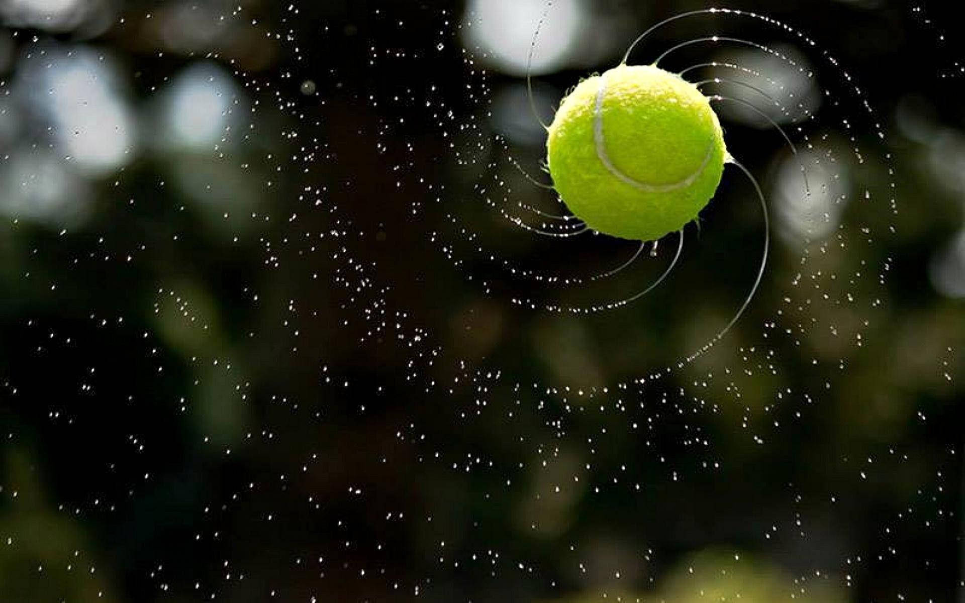 Tennis 桌布 壁紙 — 一顆亮黃色的網球懸浮在半空中，帶有水珠和運動軌跡，背景是模糊的綠色。