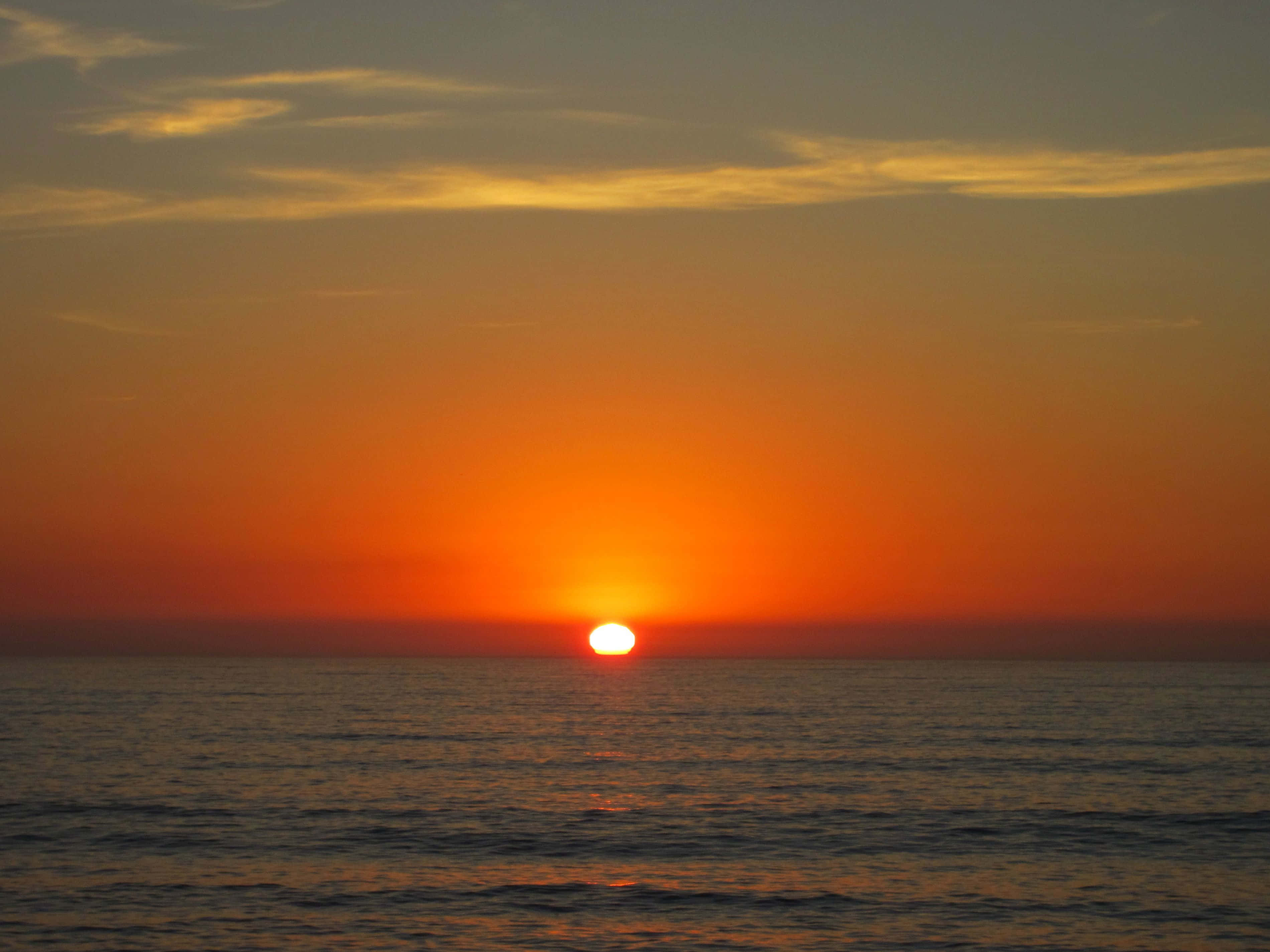 Sunset Ocean 桌布 壁紙 — 一顆充滿活力的橙色太陽在漸變天空下沉入平靜的海平線。