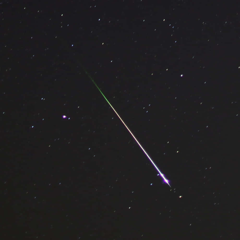 meteor 桌布 壁紙 — 一顆充滿活力的流星斜斜地劃過繁星點點的夜空，留下一條發光的綠色和紫色痕跡。