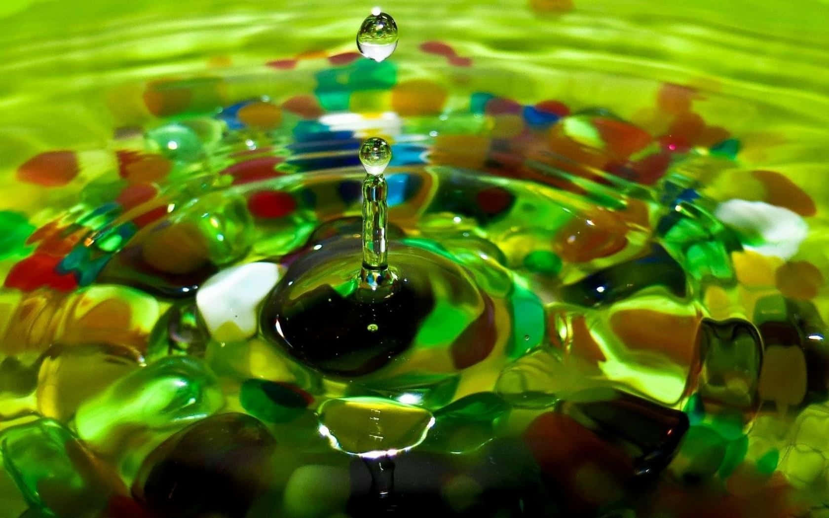 Water Drop 桌布 壁紙 — 一顆充滿活力的綠色水滴懸浮在漣漪表面之上，反射出五彩繽紛的玻璃珠。