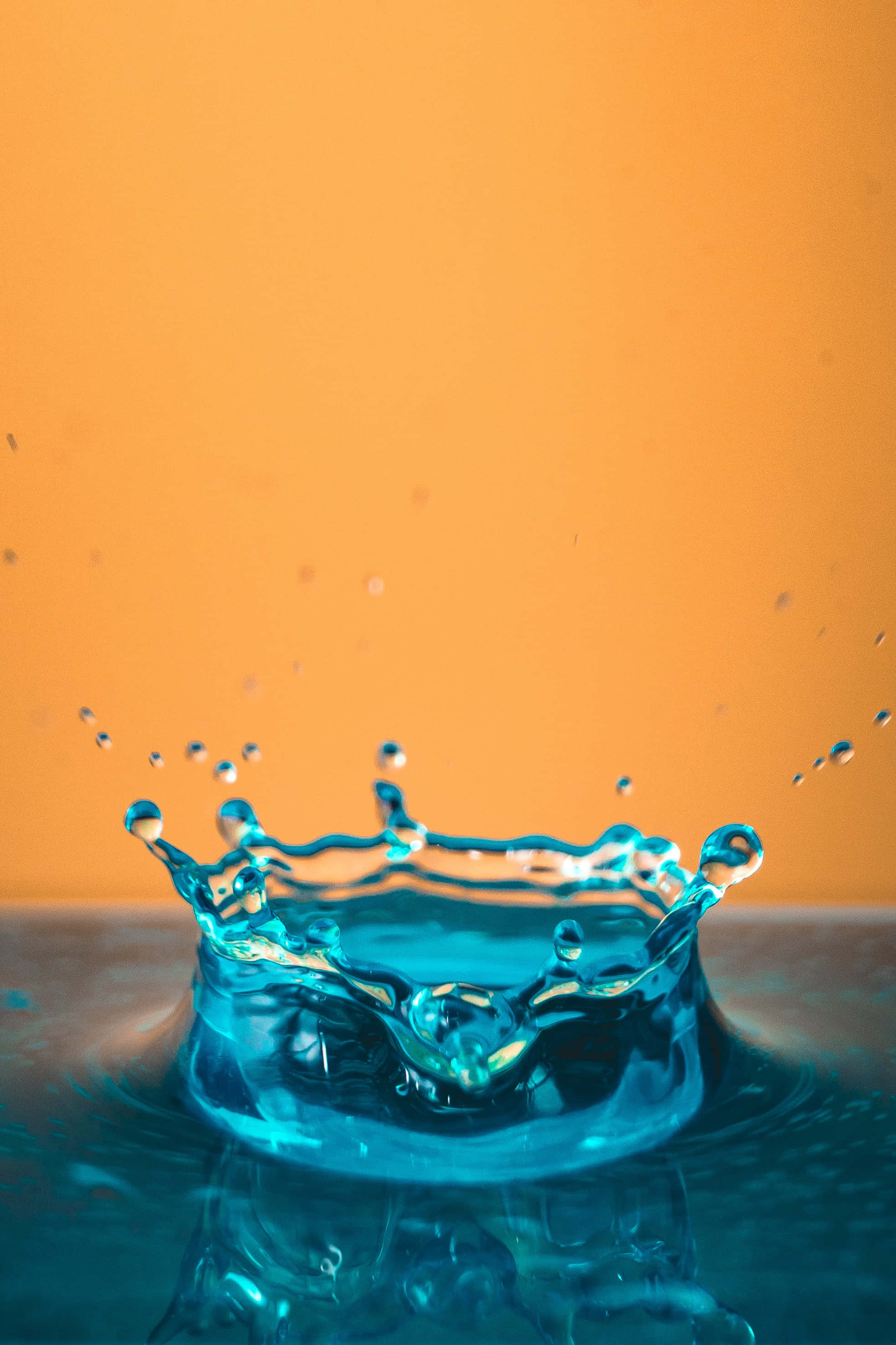 Splash 桌布 壁紙 — 一顆充滿活力的藍色水珠在溫暖的橙色背景上向上飛濺，形成一頂閃閃發光的水珠皇冠。