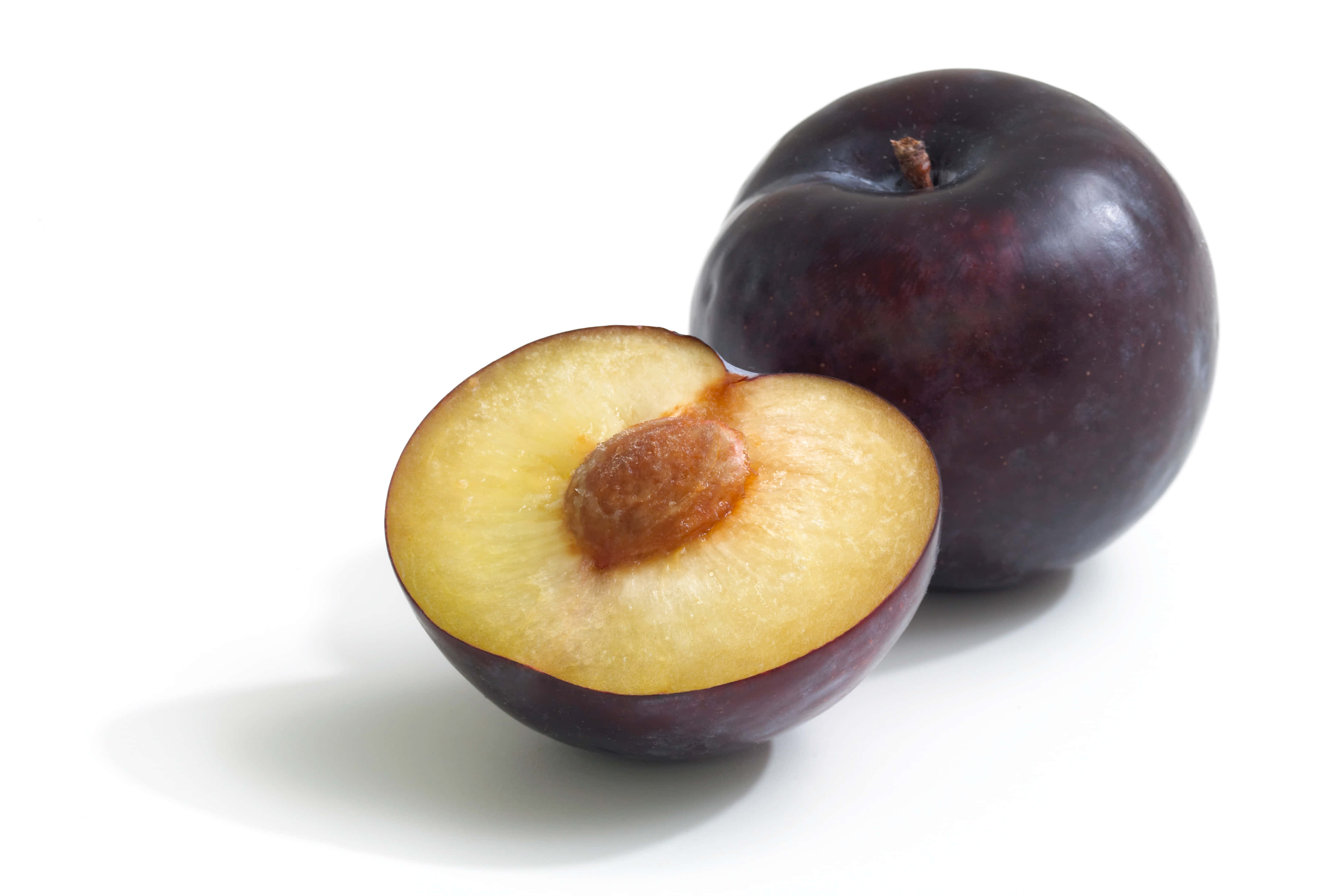 Purple Plums 桌布 壁紙 — 一顆光滑的深紫色李子切成兩半，露出淡黃色的果肉和棕色的果核，背景是純白色。