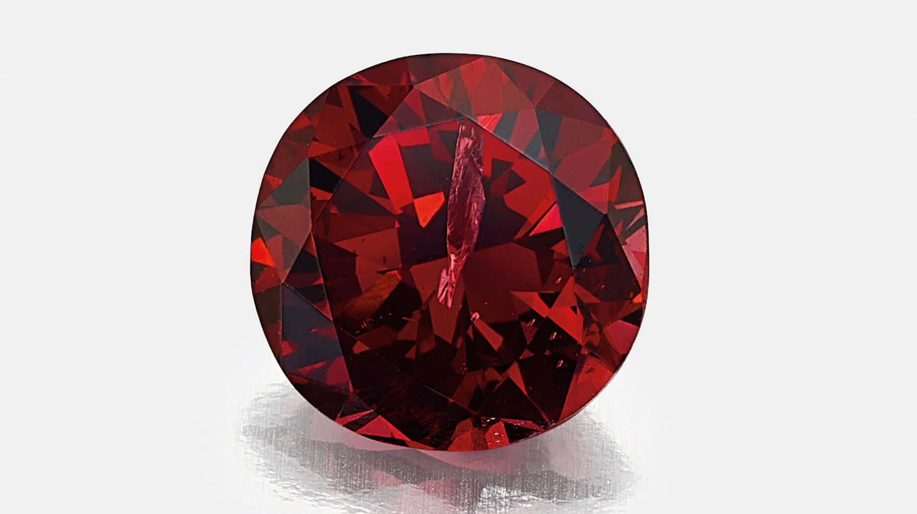 Red Diamond 桌布 壁紙 — 一顆切割璀璨的深紅色寶石，在柔和的白色背景上閃耀著火彩般的刻面。
