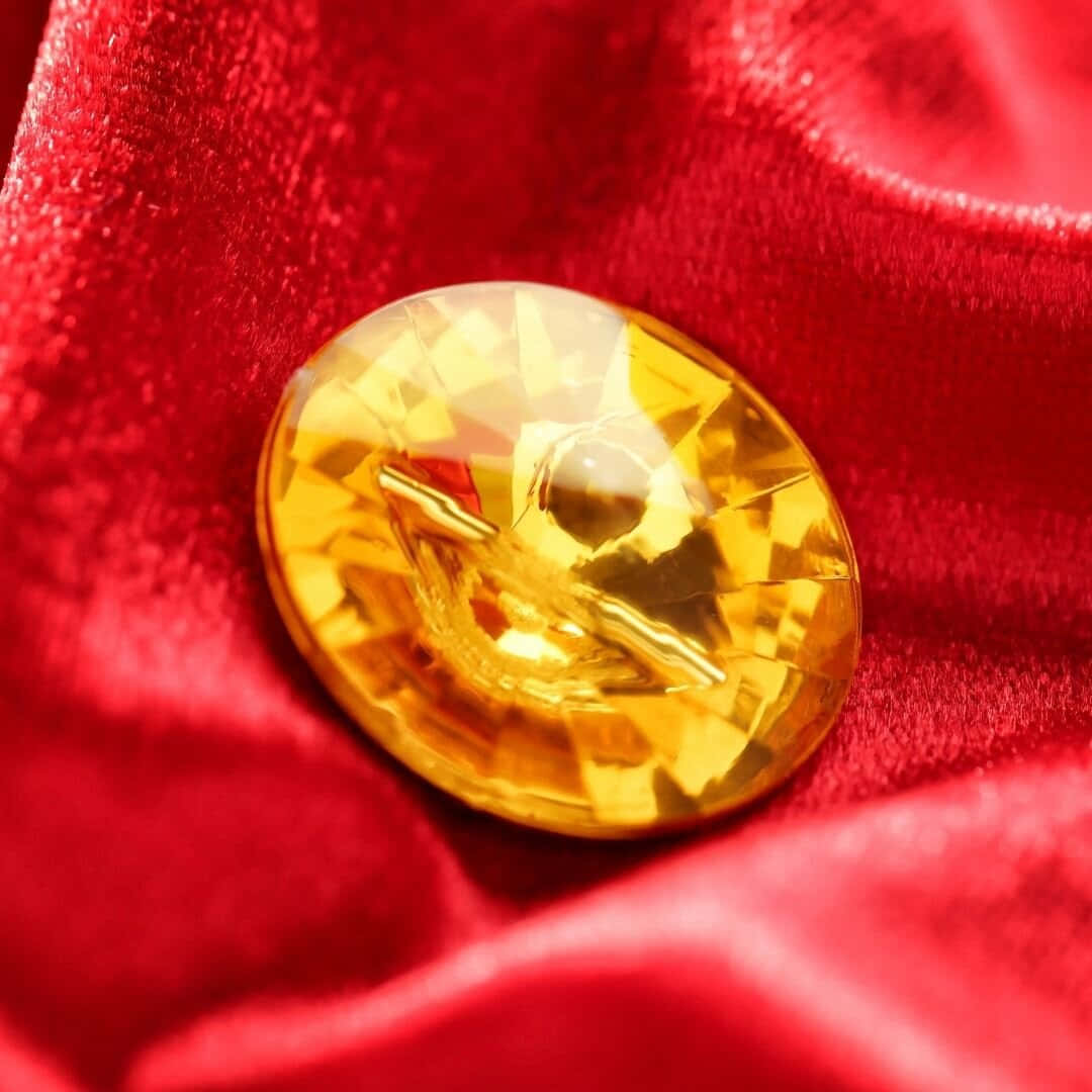 Yellow Sapphire 桌布 壁紙 — 一顆切割面金色黃水晶寶石，置於質感豐富的紅色天鵝絨布料上，布料帶有柔軟皺褶和閃爍高光。